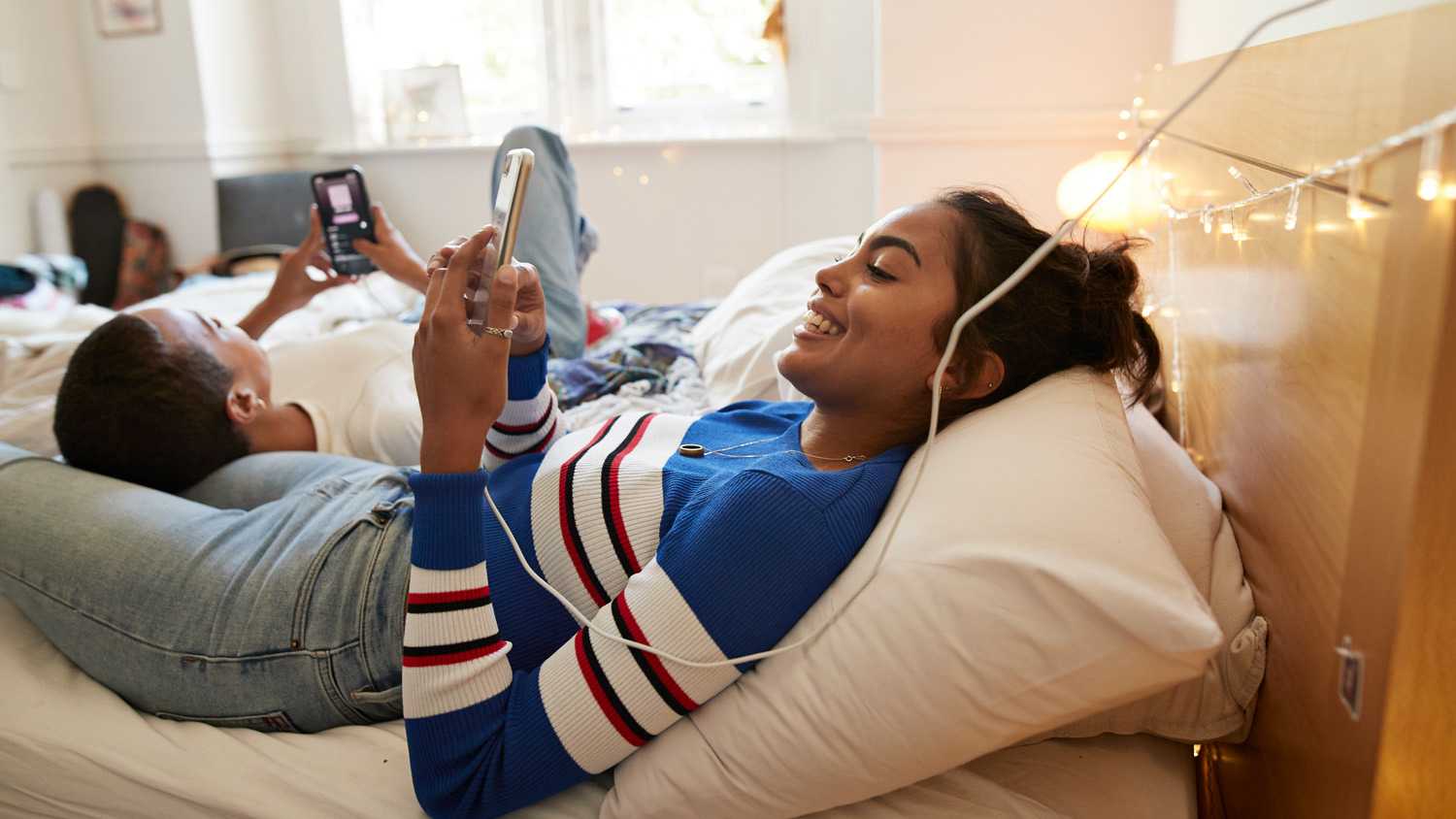 Smiling woman using mobile phone with friend on bed