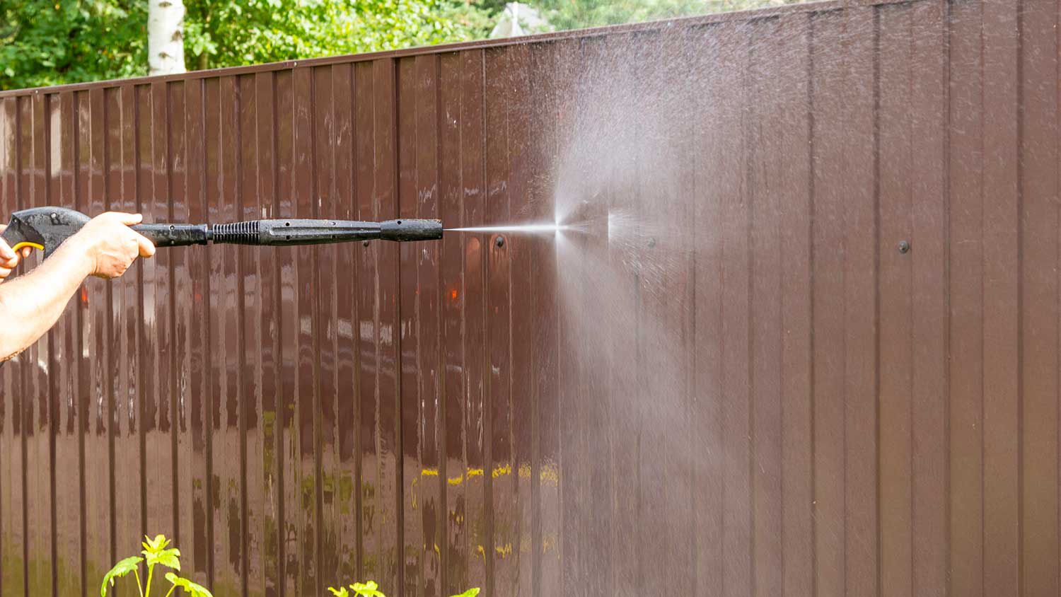 Closeup of a man using pressure washer to clean patio fence