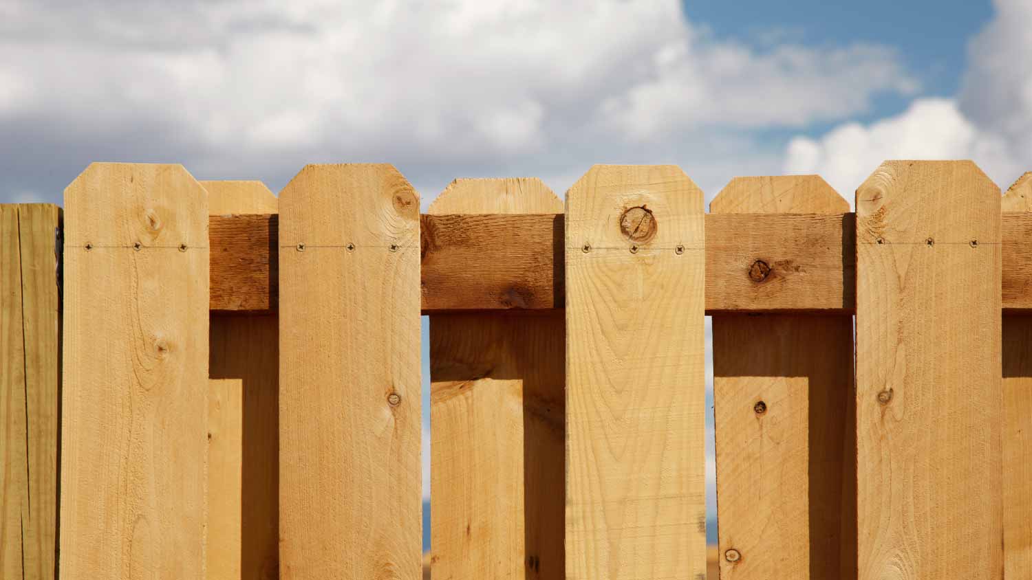 A cedar board-on-board picket fence and a cloudy blue sky