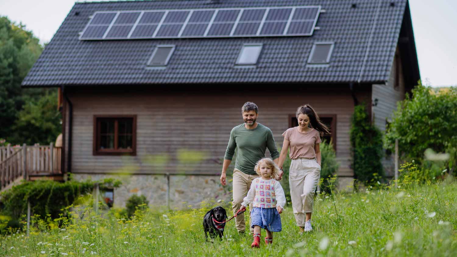 A family with their dog in front of their home with solar panels