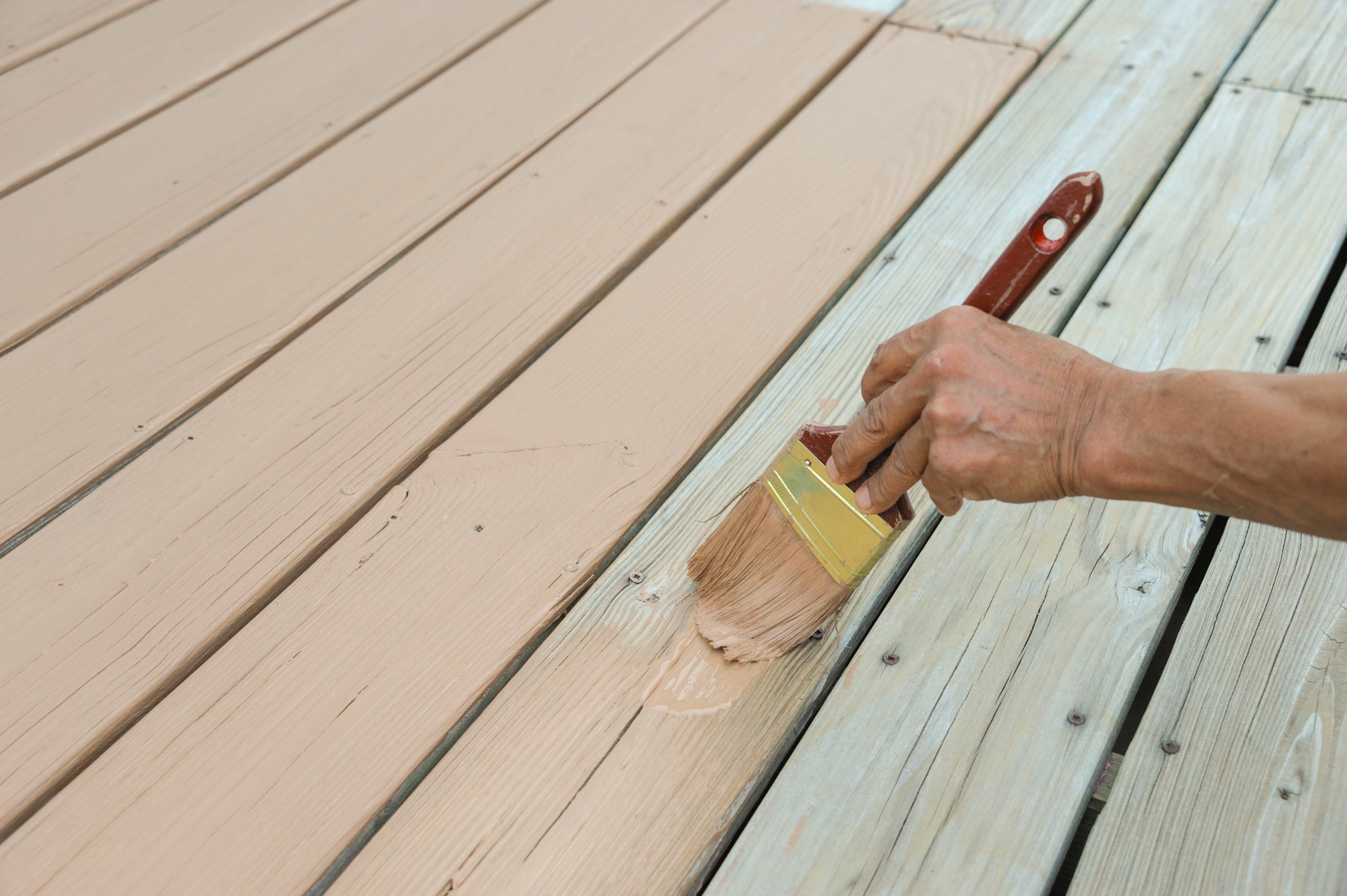 Handyperson using a brush to paint wooden deck boards