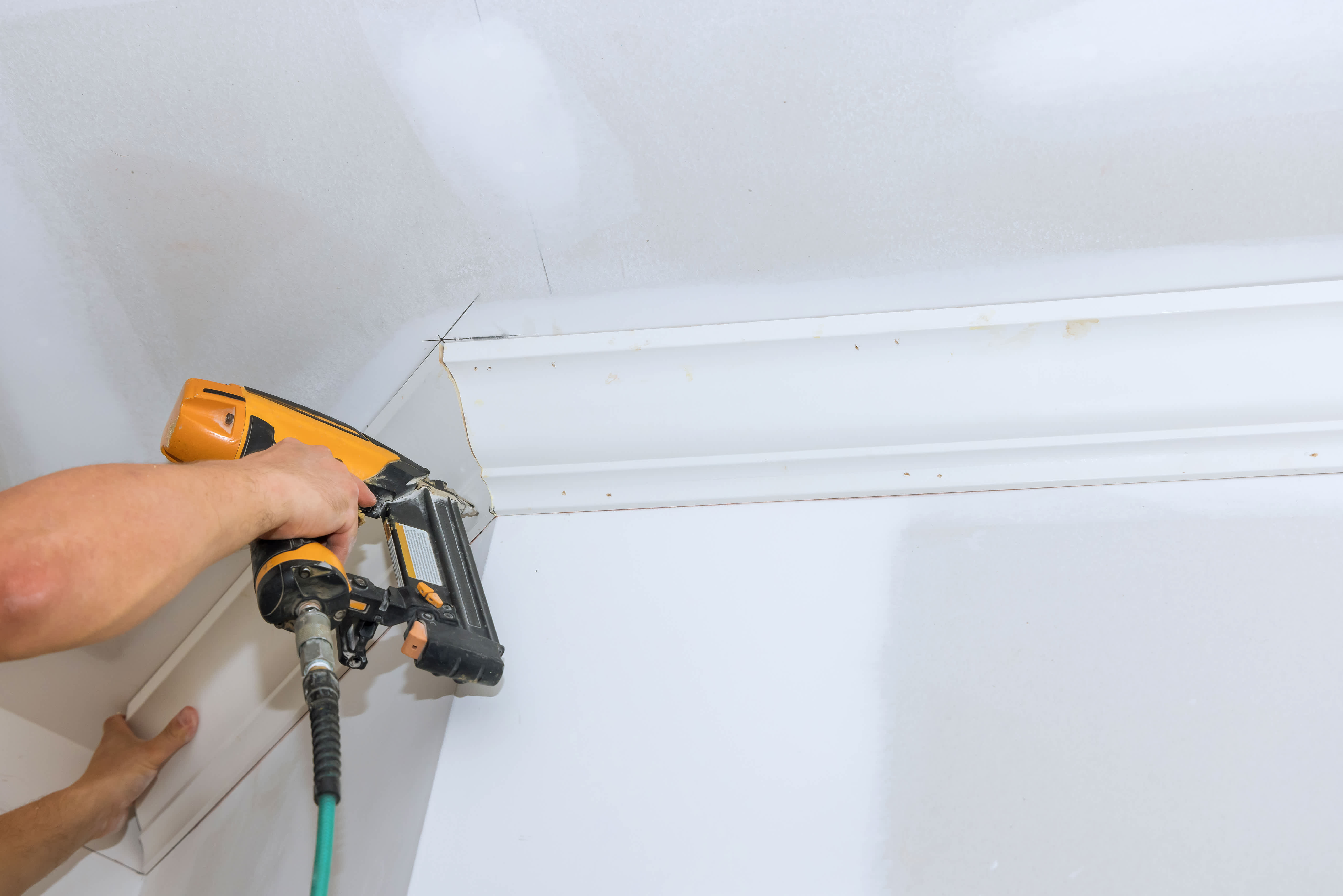 A person installing a crown molding with a nail gun