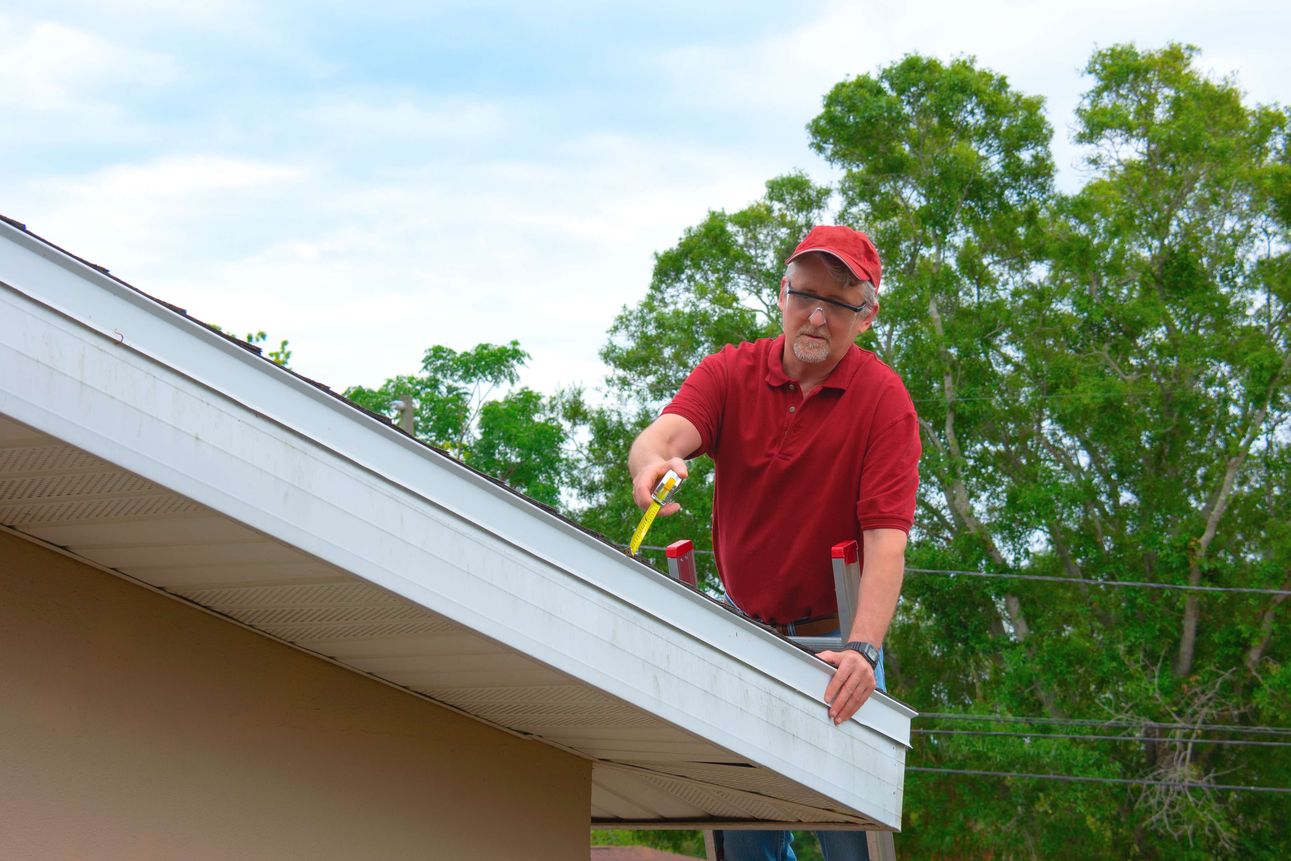 Handyperson using a measuring tape to calculate the size of the roof