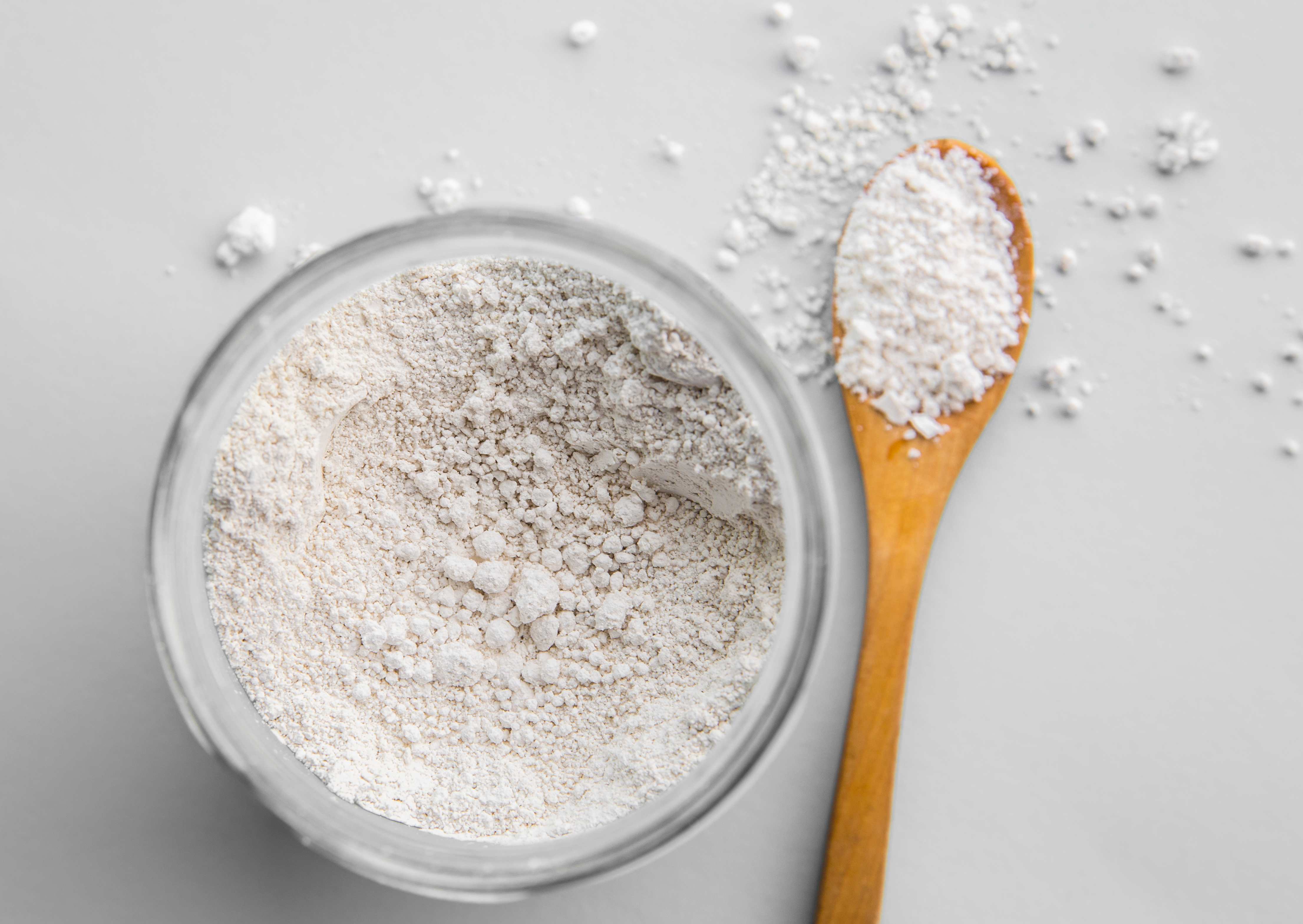 Diatomaceous earth powder in a glass container and a wooden spoon