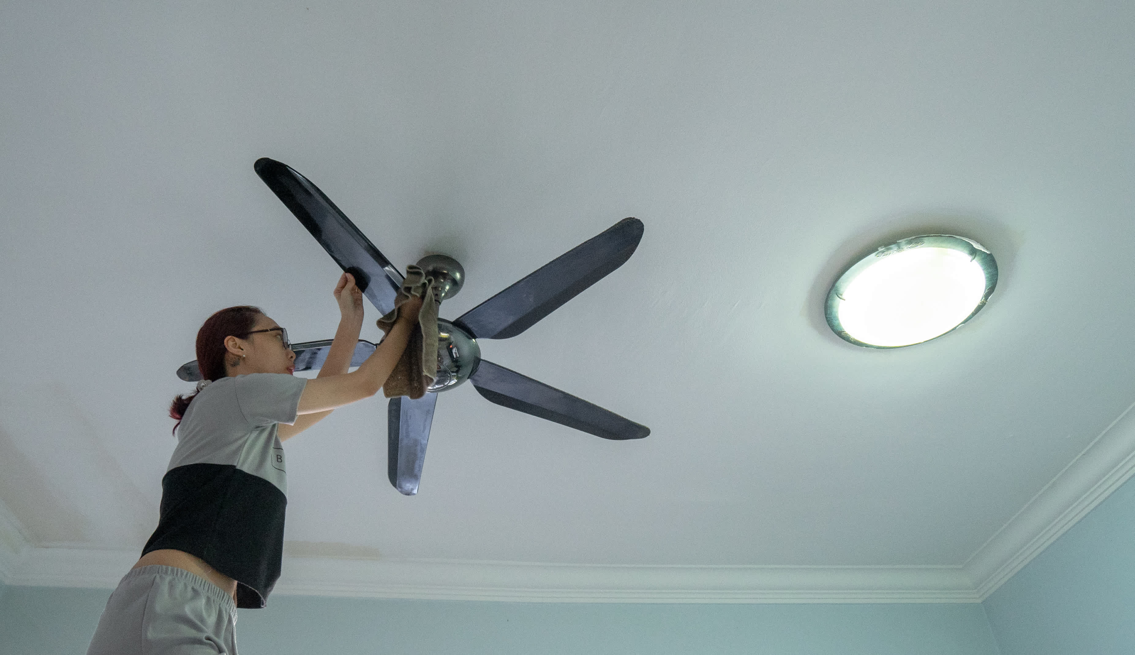 Woman using a cloth to clean a ceiling fan