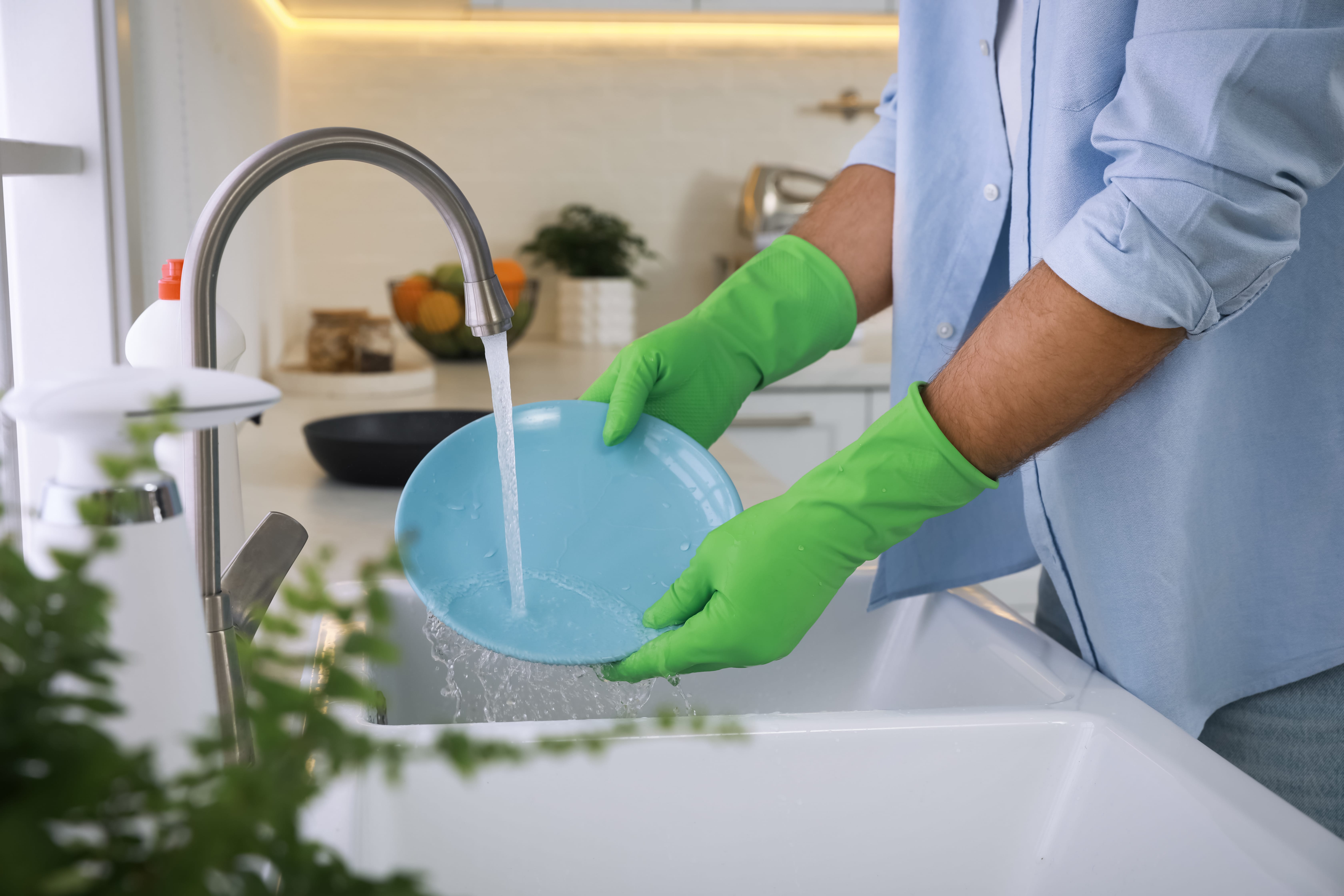 A man wearing rubber gloves washes dishes in the kitchen sink