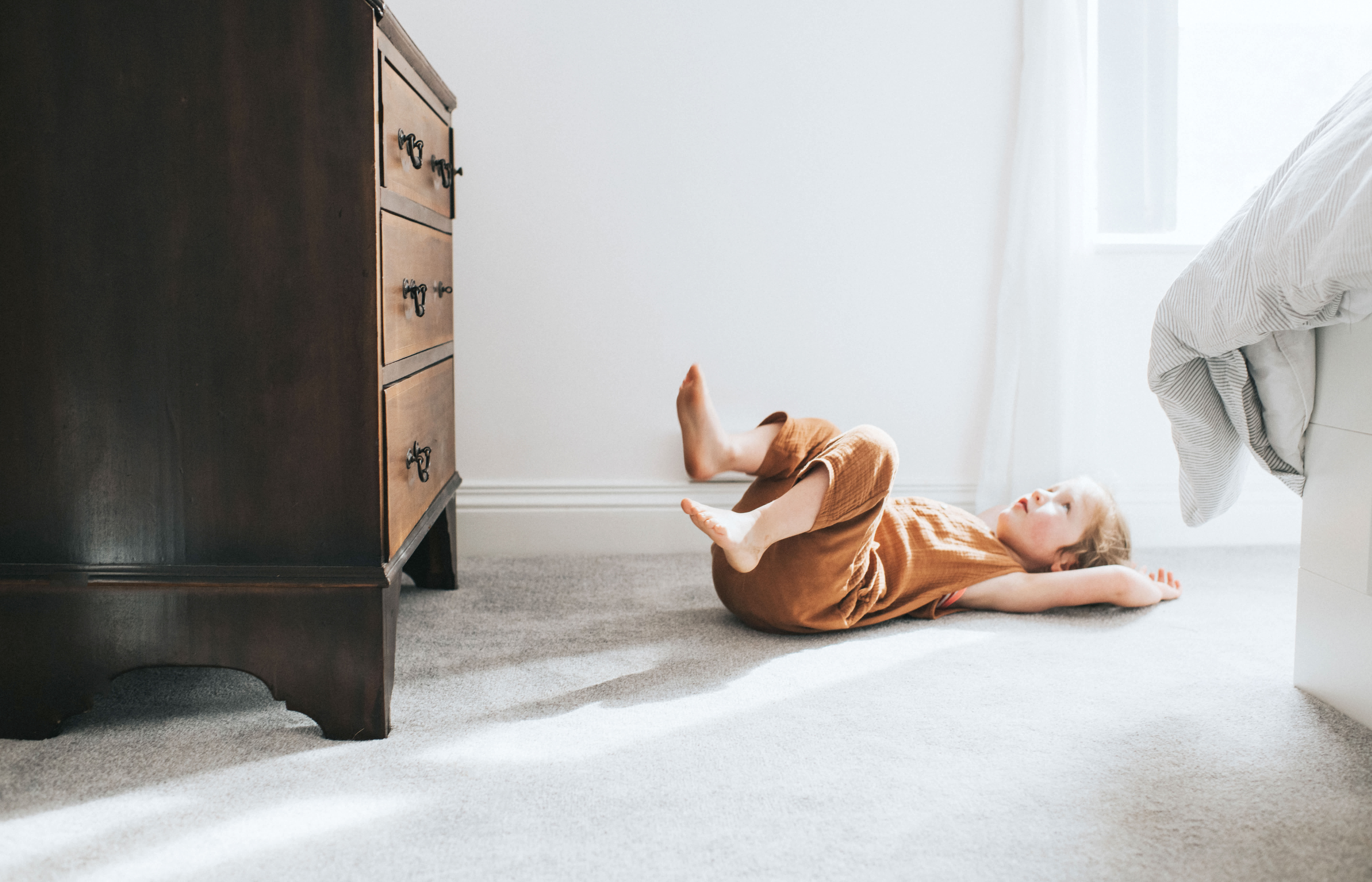 Girl lying down on a gray carpet in a bright bedroom