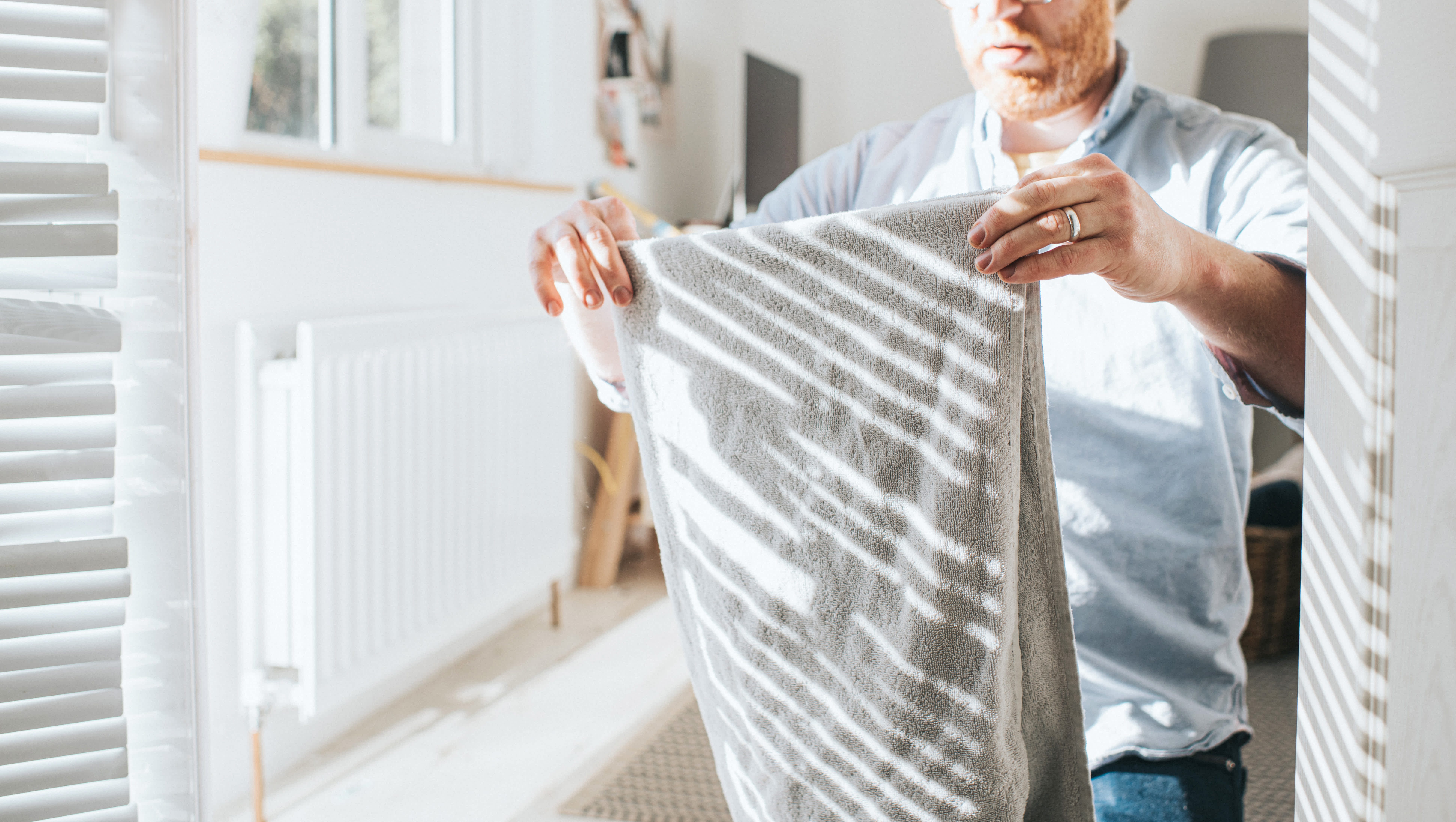 Man in a bright room is folding a gray towel