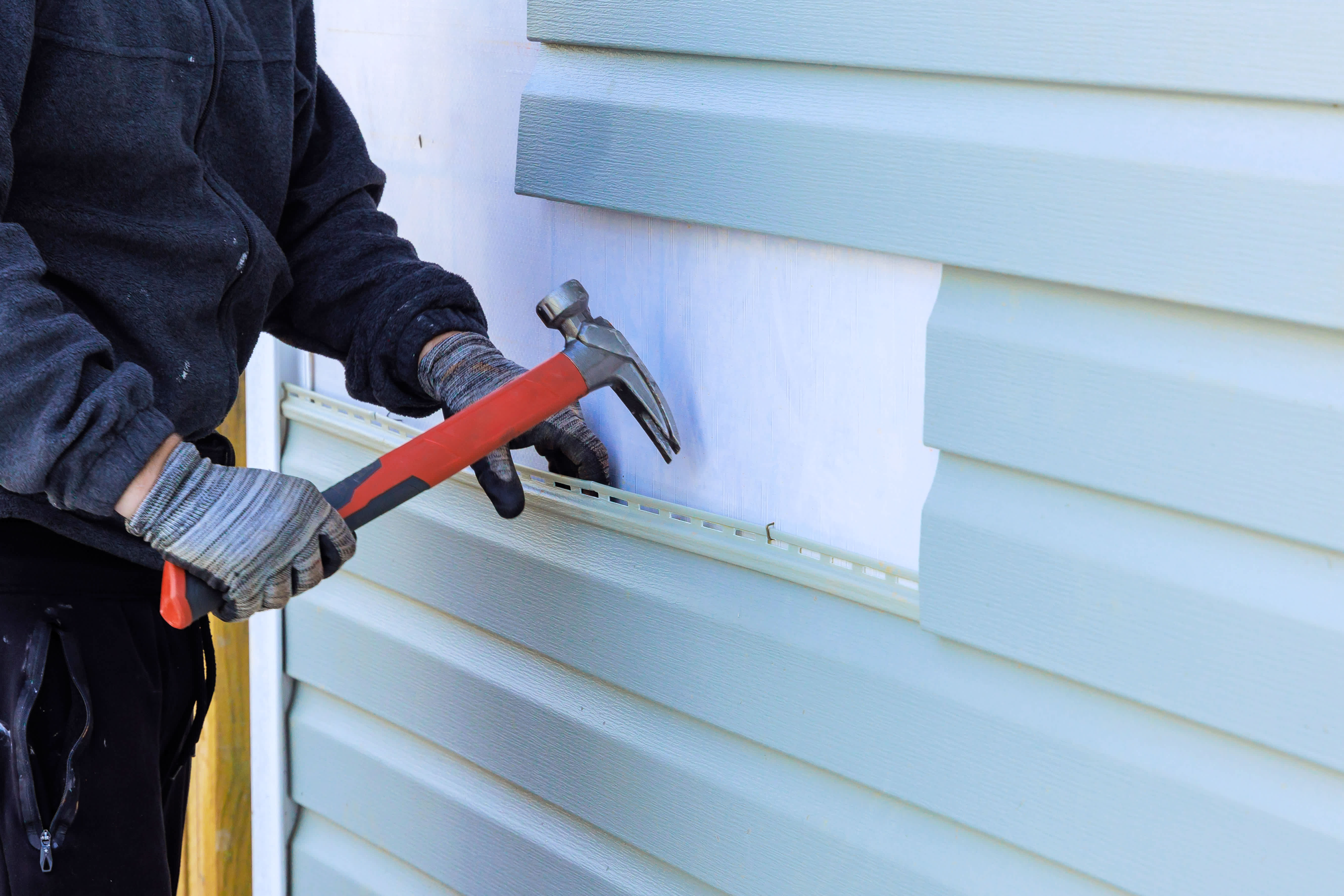Worker removing old vinyl siding from the house