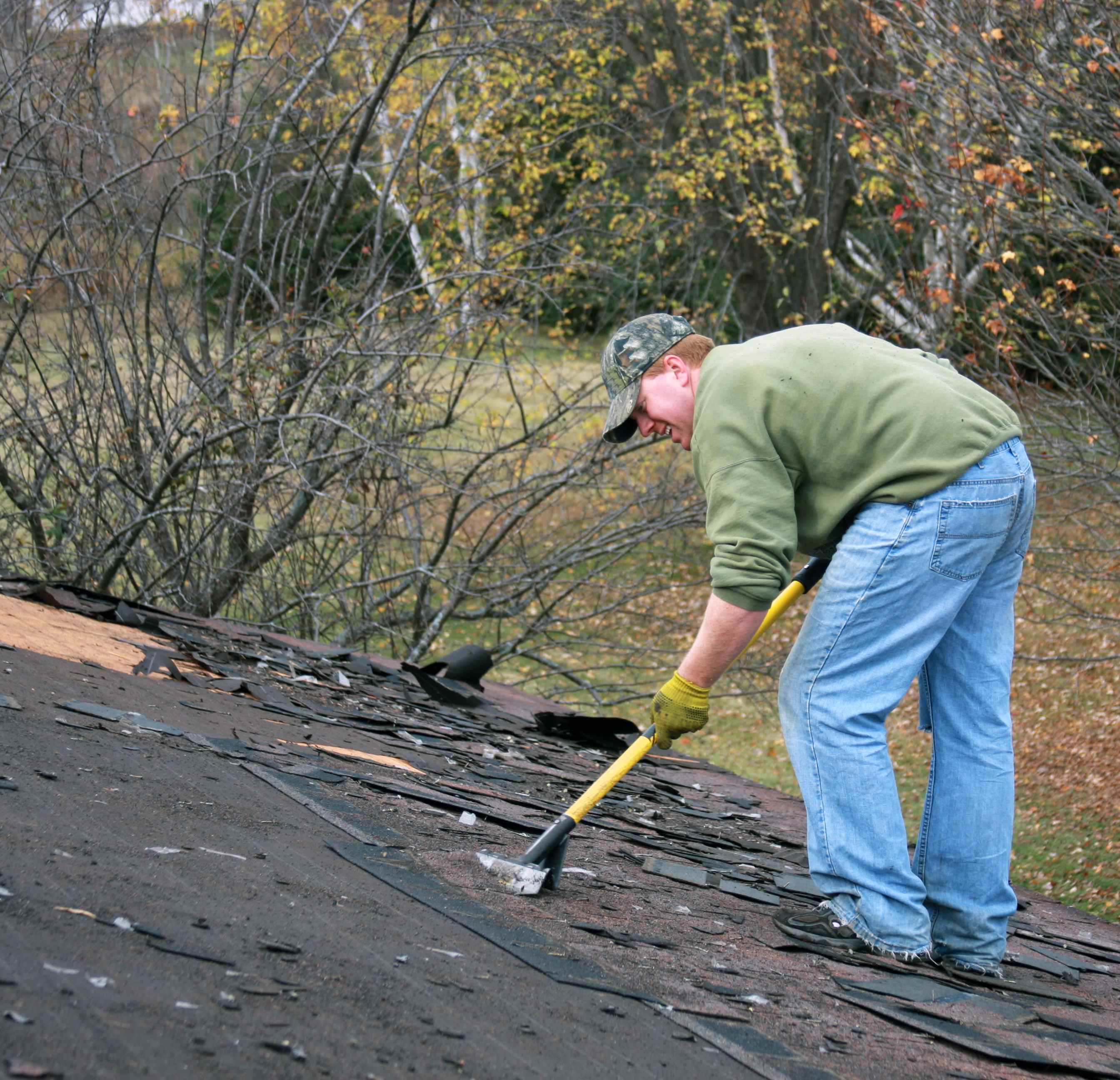 Roofer removing old asphalt shingles from the roof