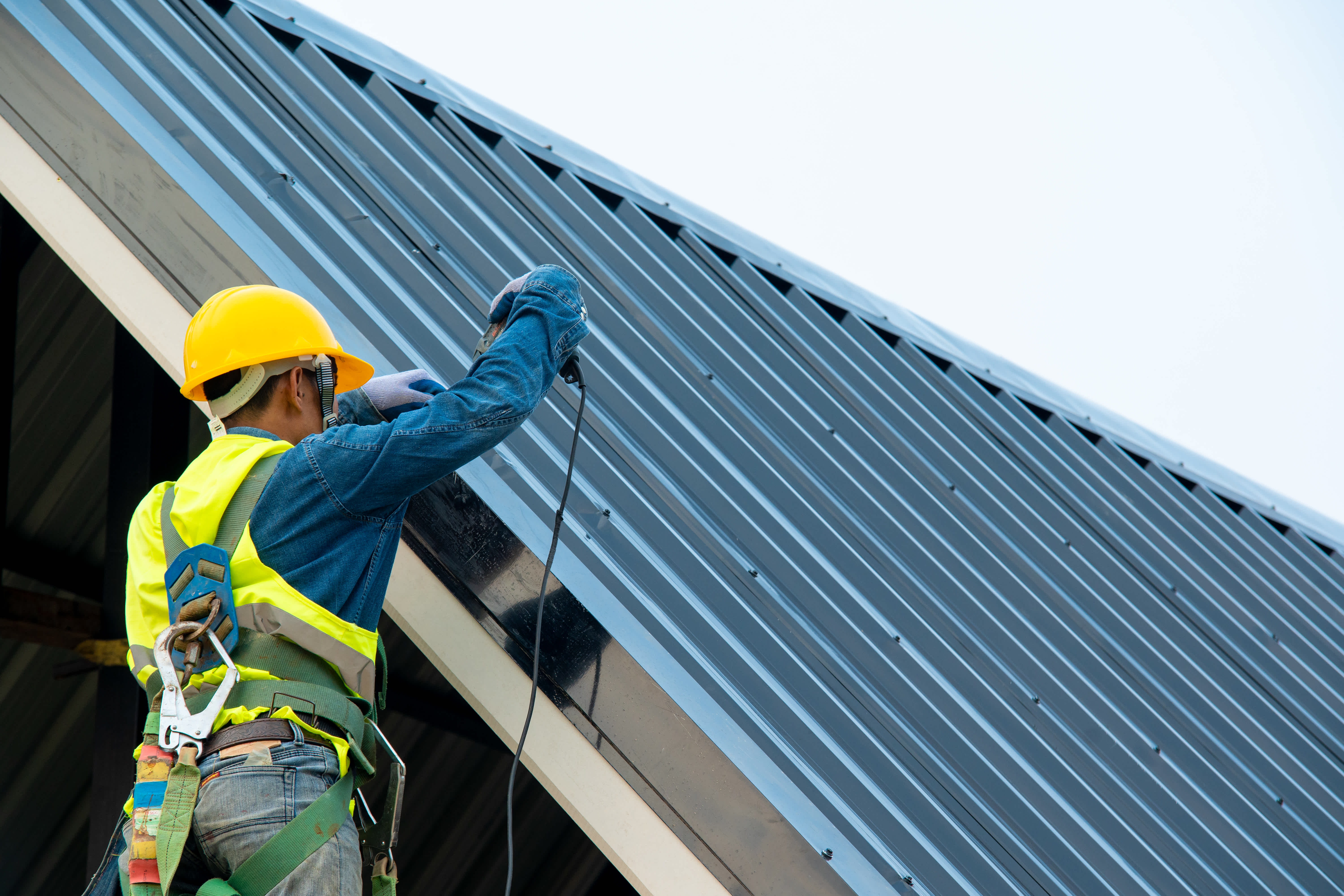 Worker wearing a safety harness repairing a metal roof