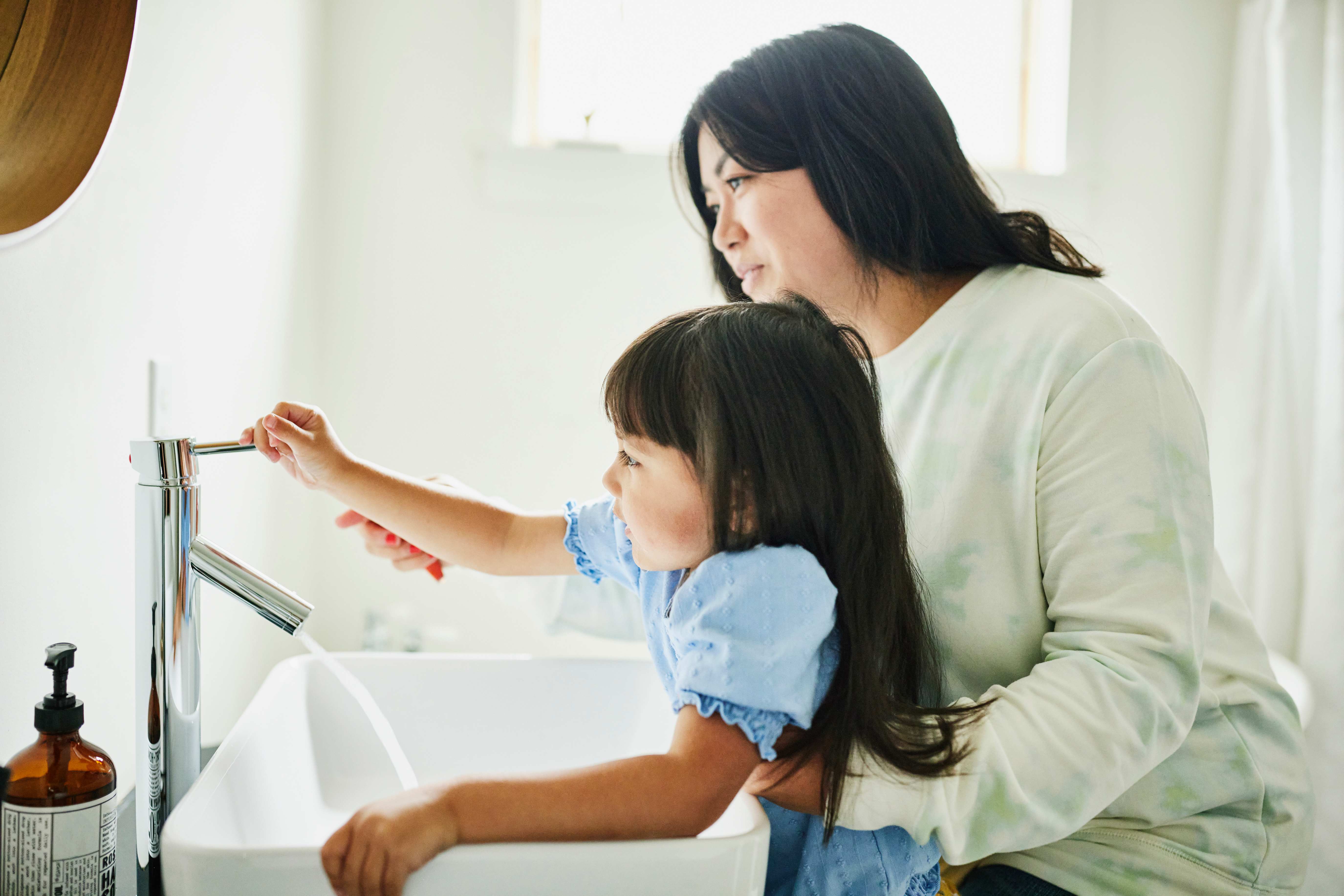 Mother helping little daughter wash her hands