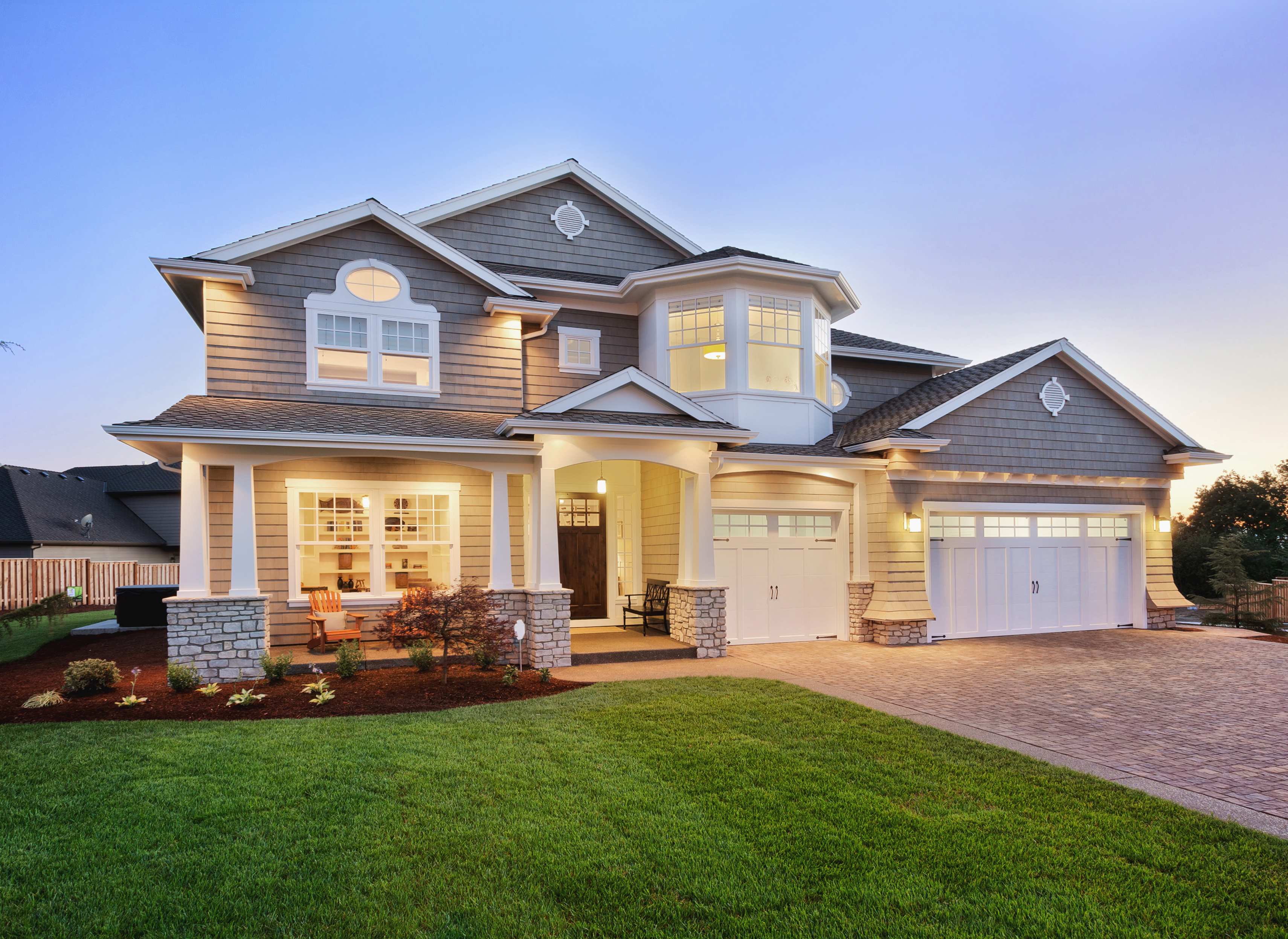 shot of front of house with outdoor light above front door, with light streaming out of front windows into dark front yard