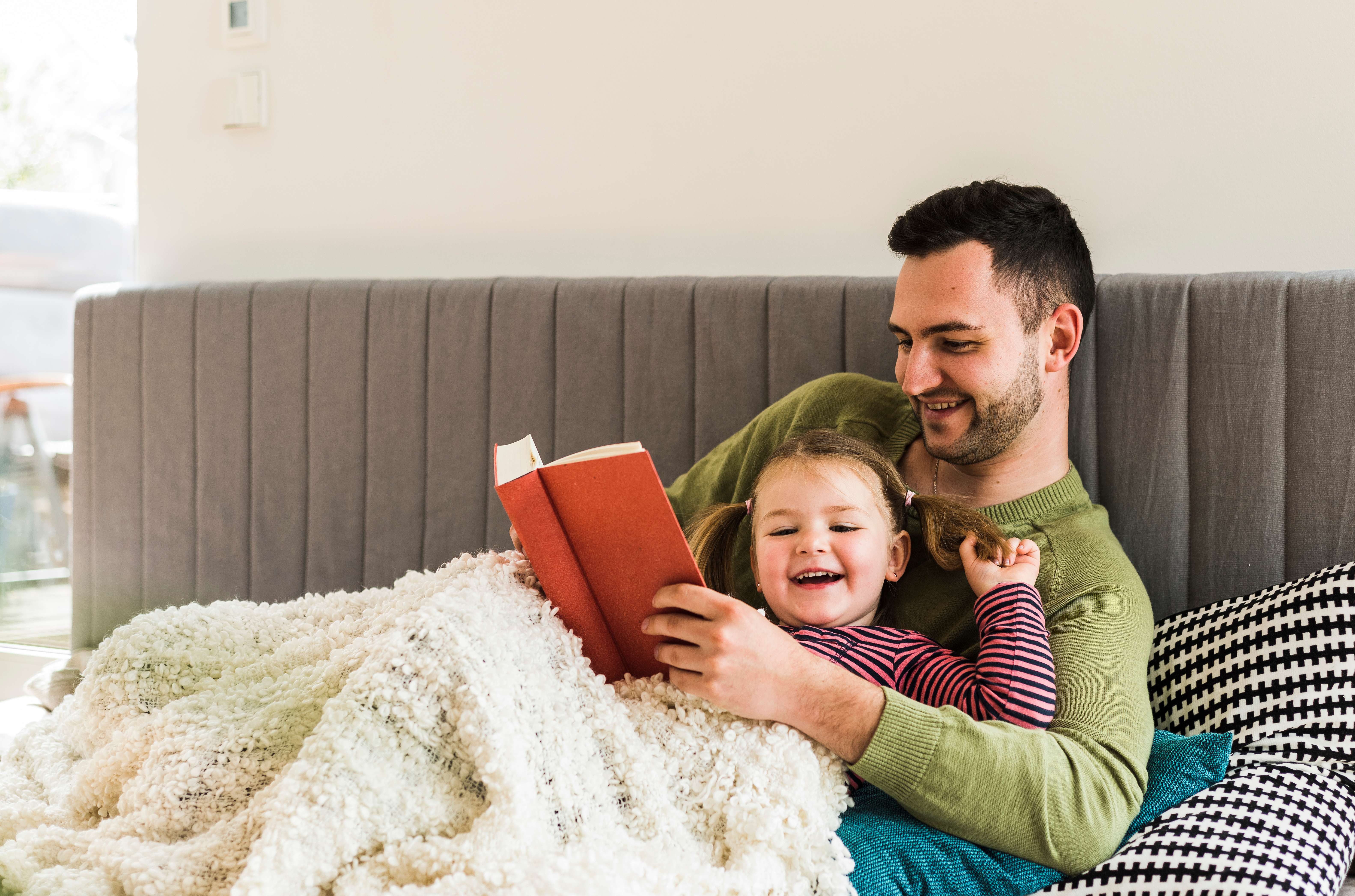 Father and daughter snuggling on the couch and reading a book