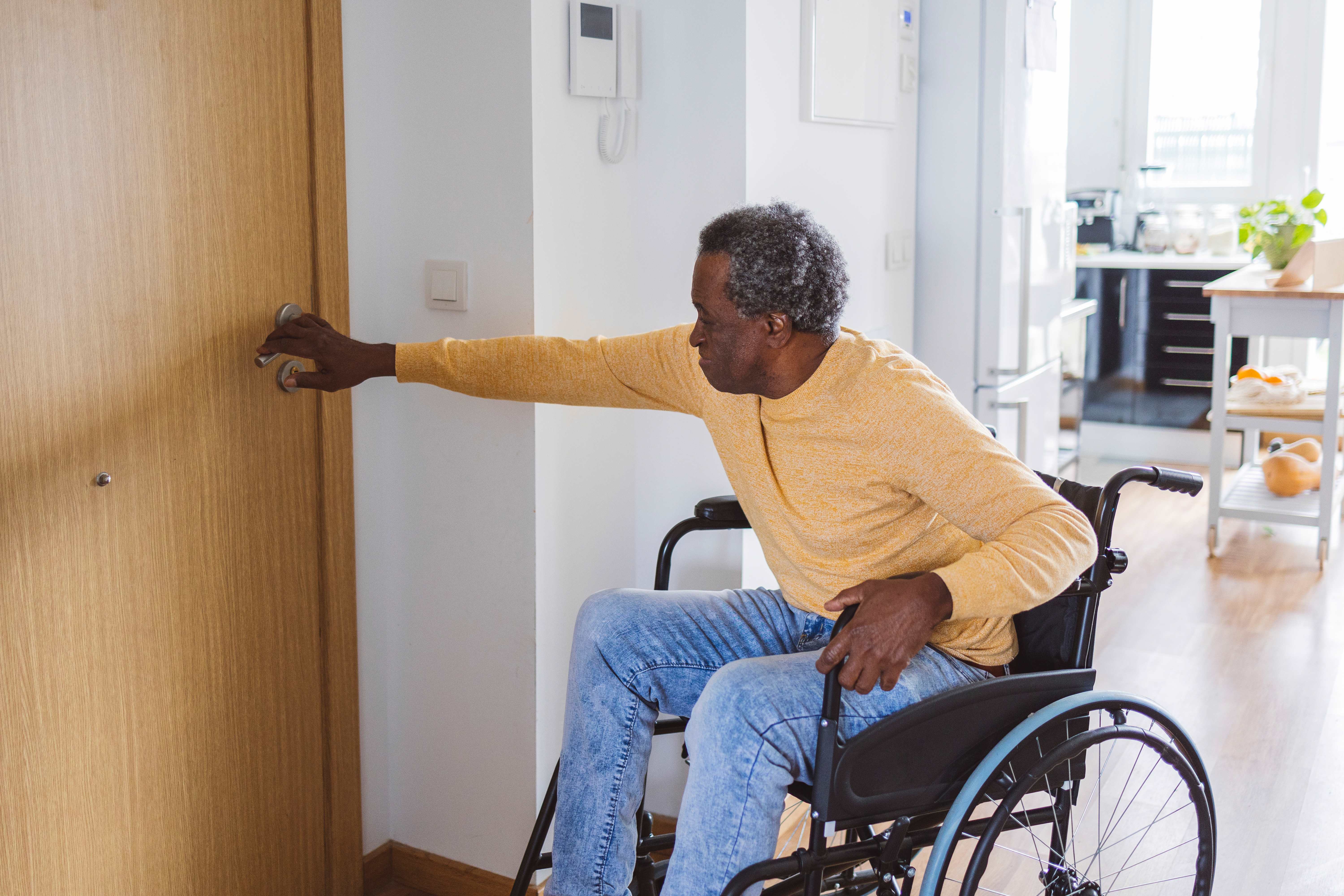 Senior man in a wheelchair opening the front door at home