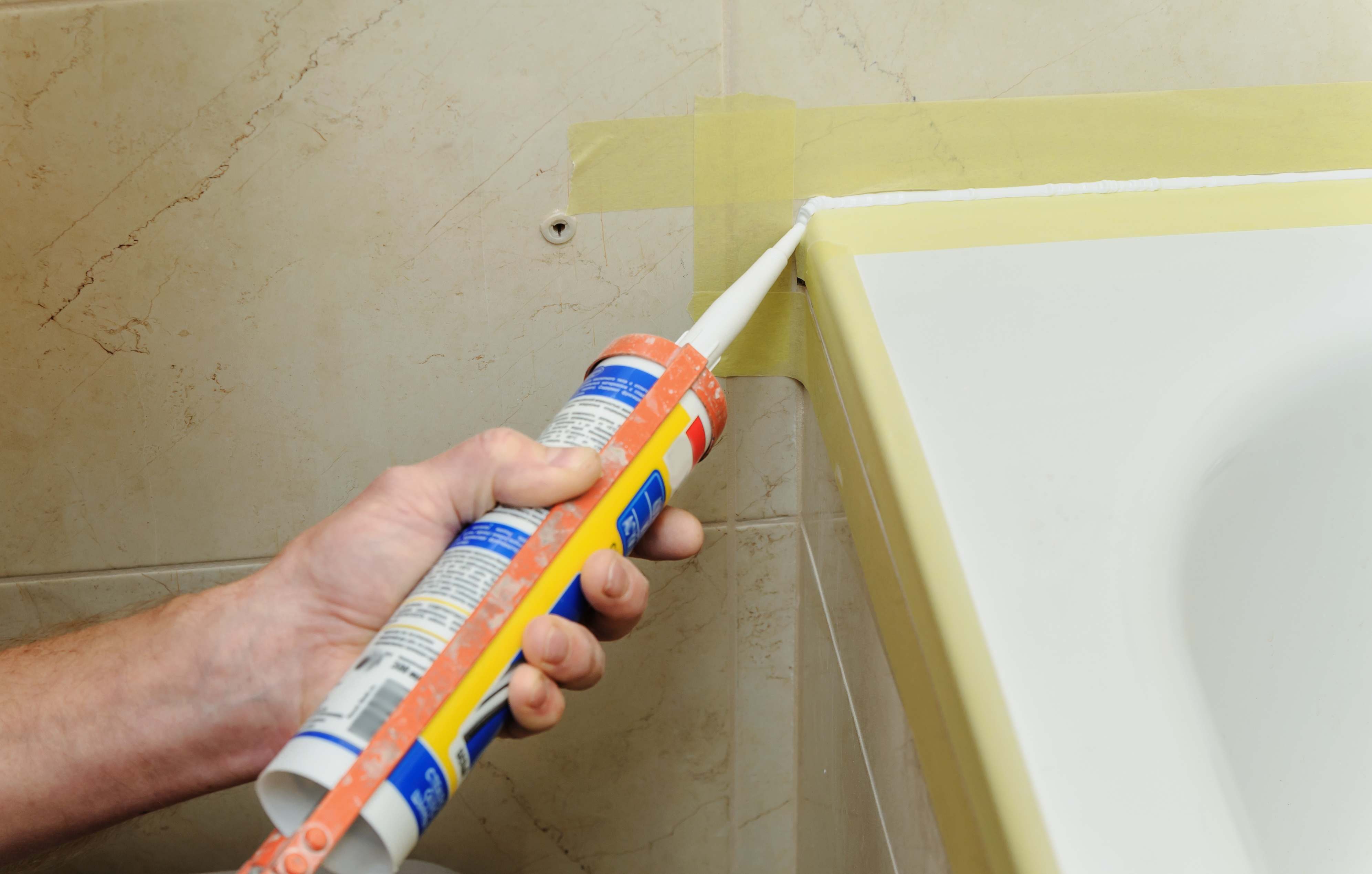 man caulking tile corners of bathtub