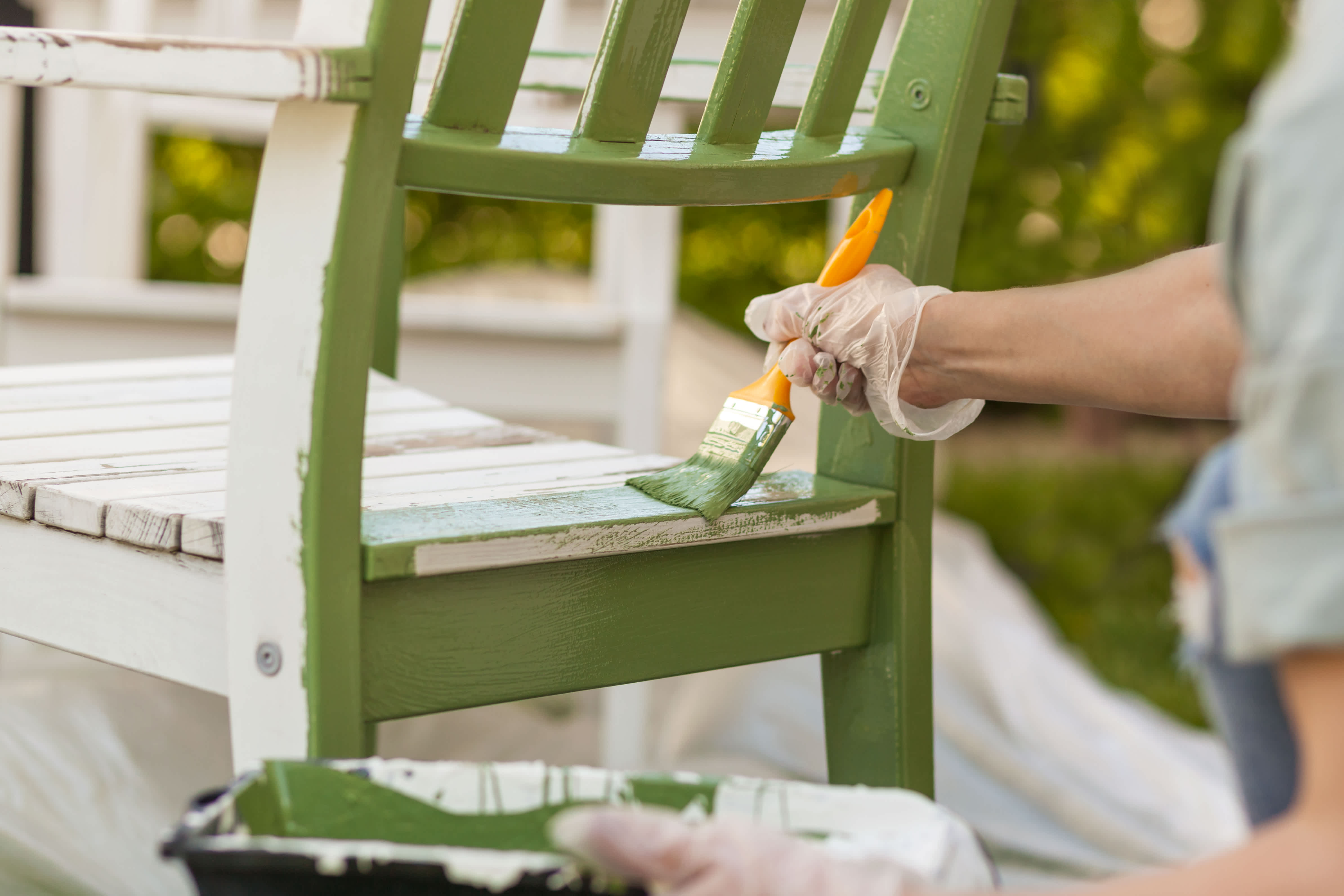 A woman painting a chair in olive green with a brush