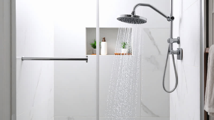 A modern shower with a rainfall showerhead releases water in a sleek bathroom with white marble tile walls.