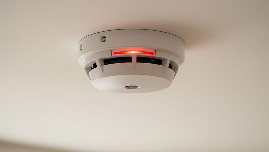 A ceiling-mounted smoke detector with a glowing red indicator light signals active status or alert mode.
