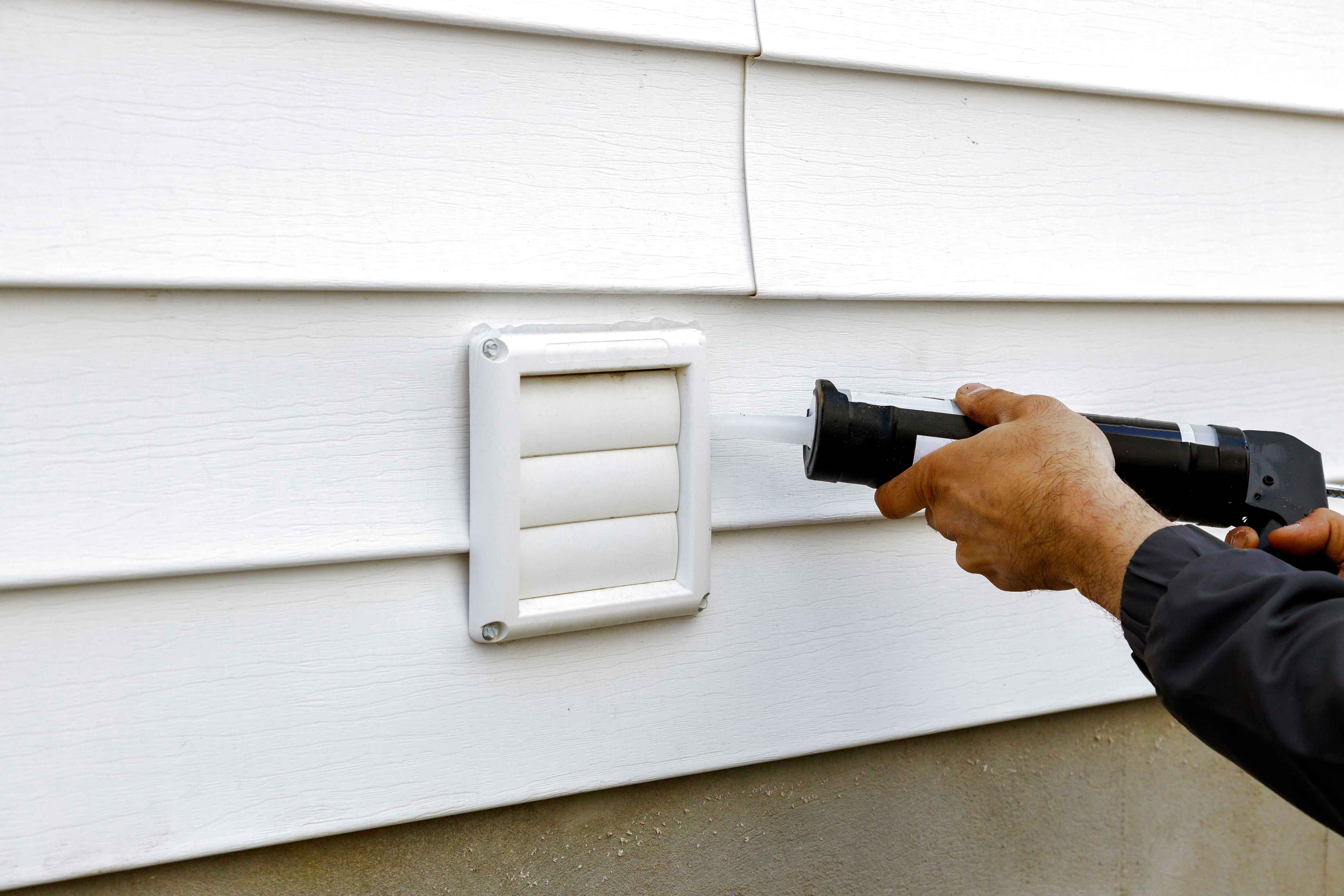man putting caulk around exhaust fan outside of home