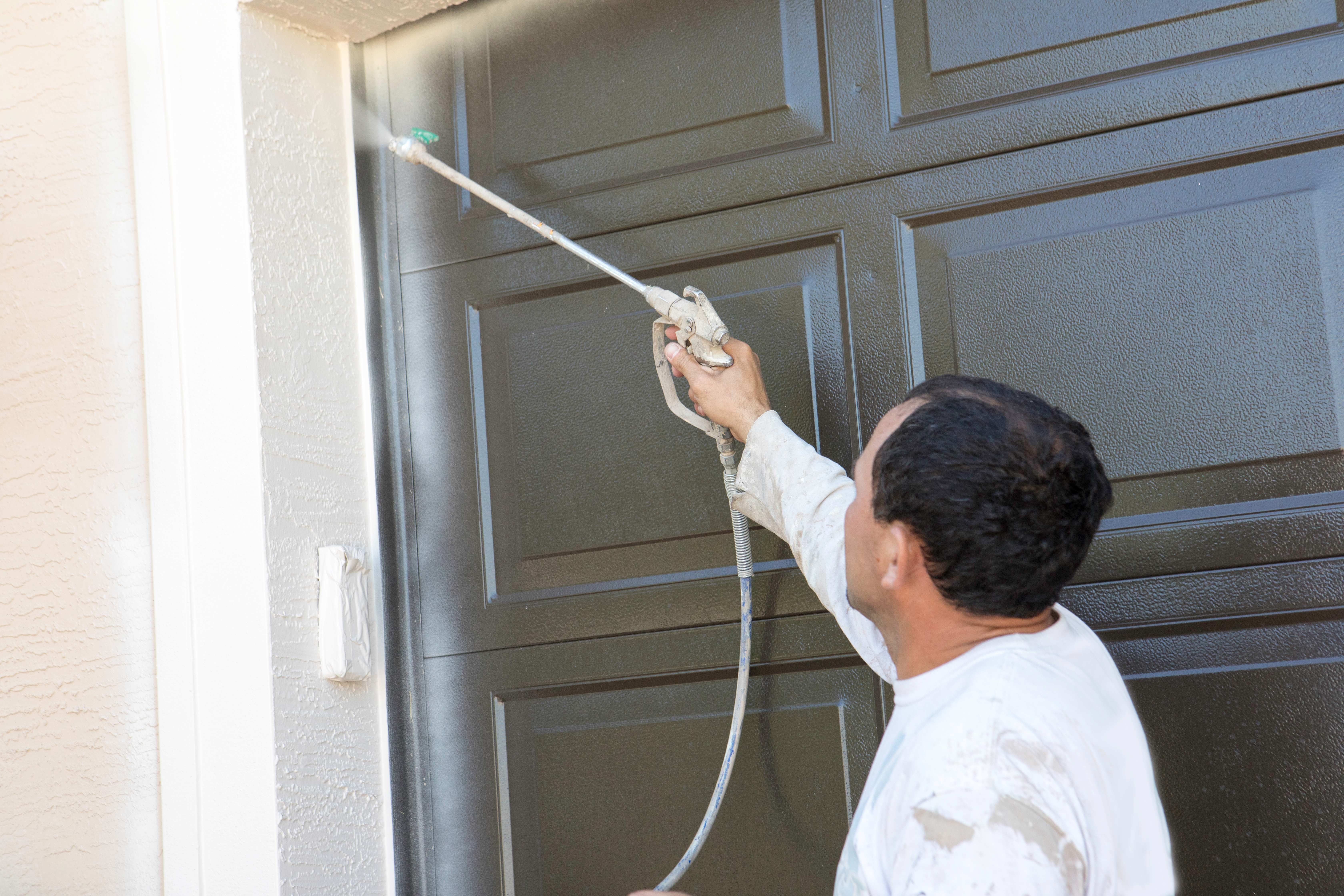 A man spray painting the exterior of a house