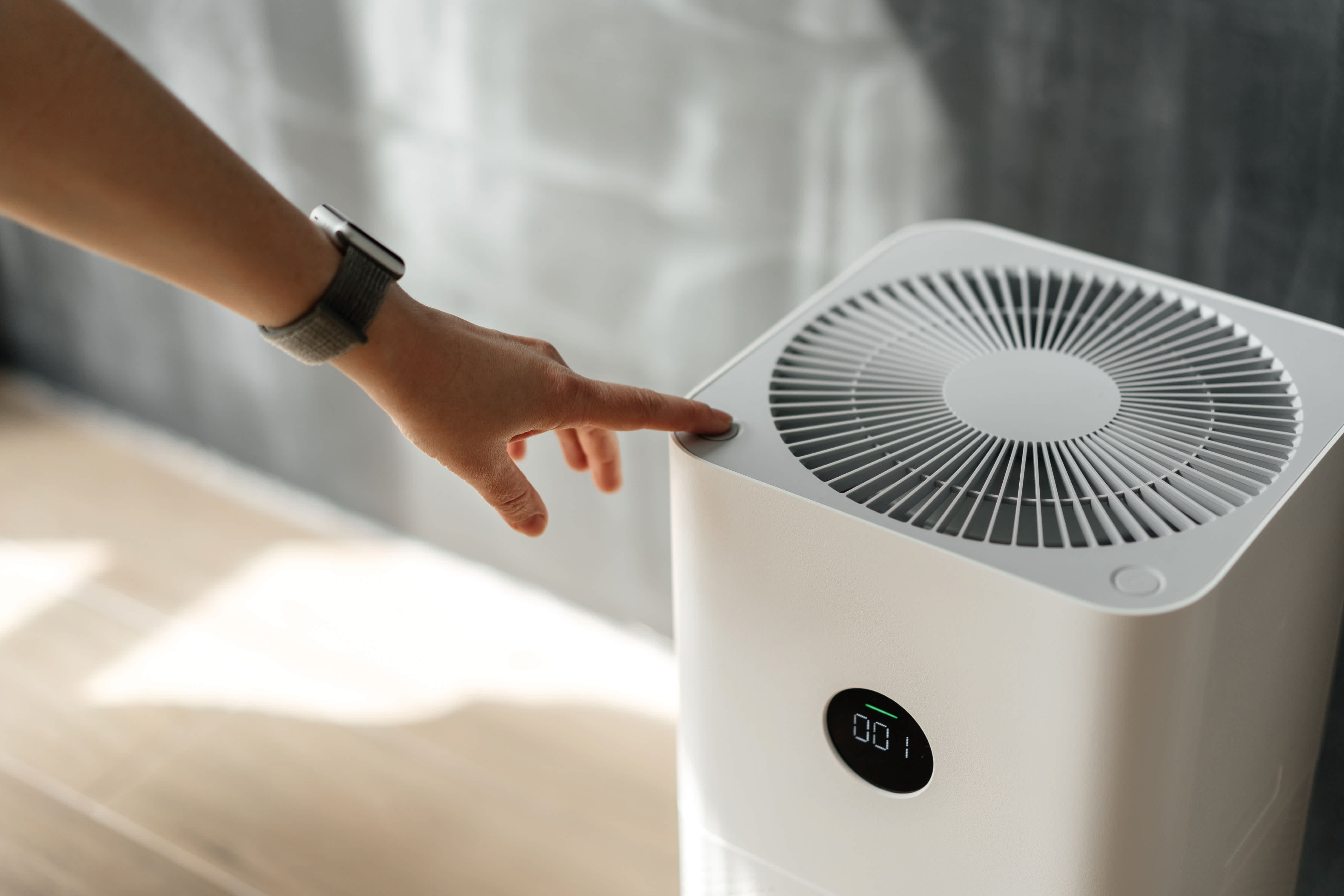 A person is pressing the power button on an air purifier