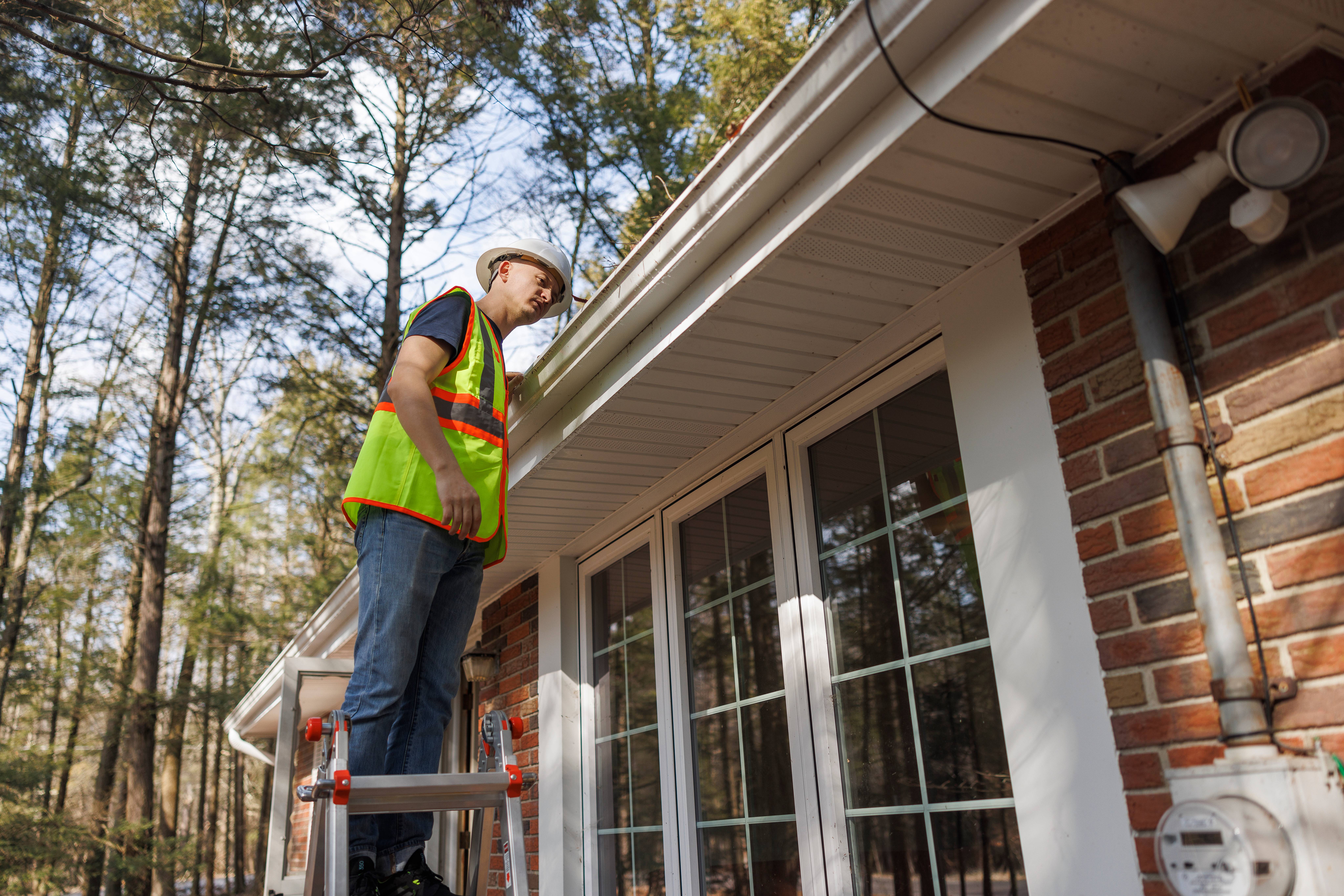 A man on a ladder inspecting a gutter
