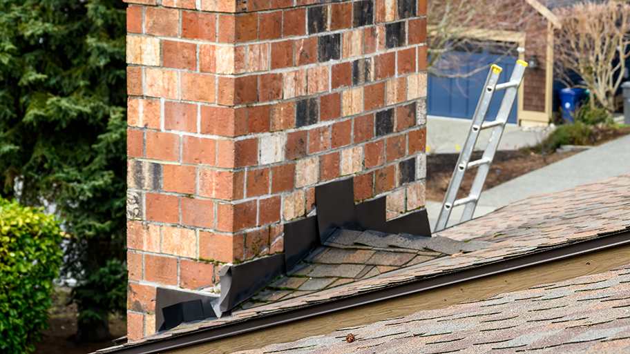 Brick chimney with a shingled roof cricket, a ladder visible in the background