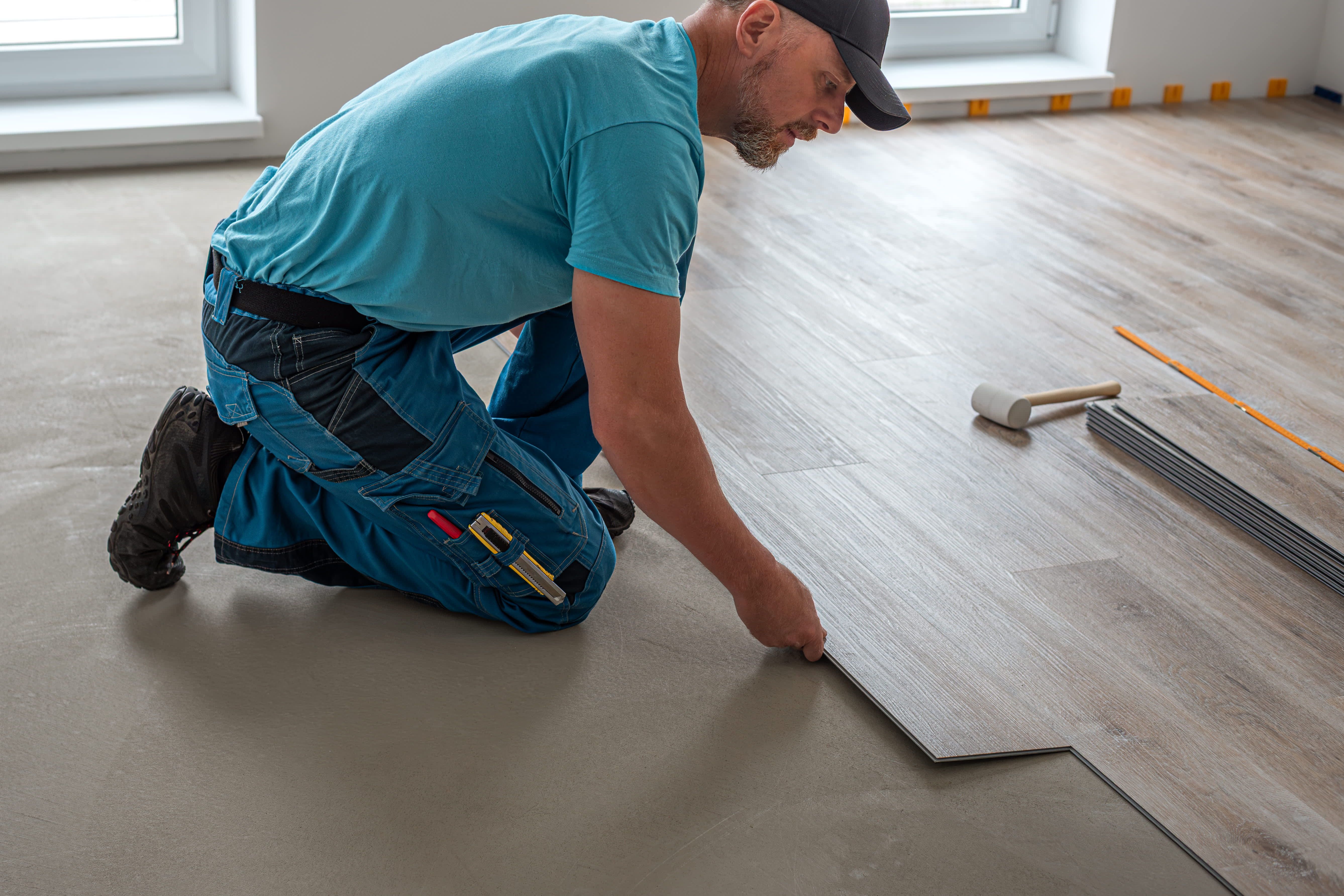 Worker installing vinyl plank floating floor with click system.