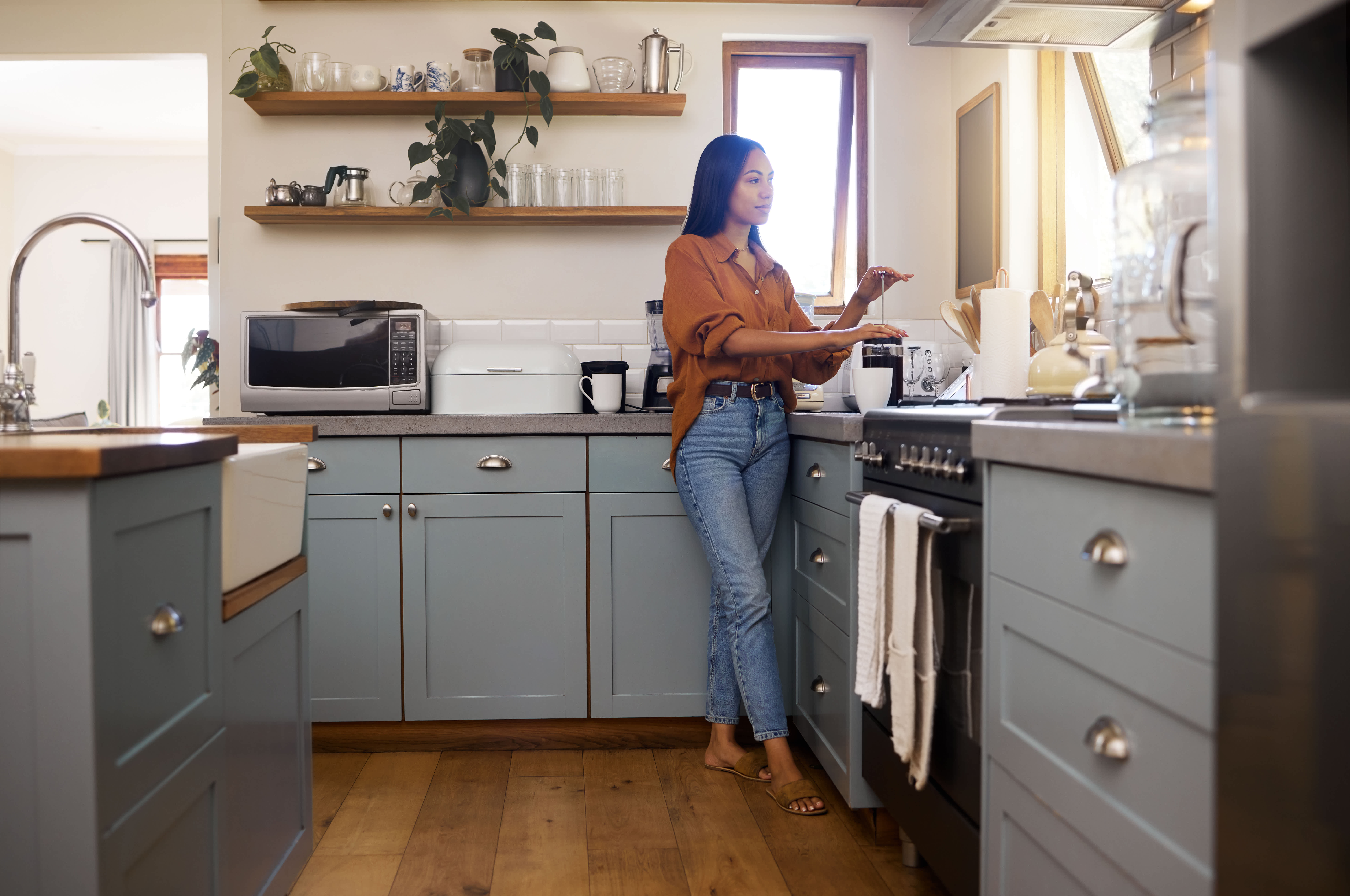 Woman making coffee in a modern kitchen with blue lower cabinets and open shelving