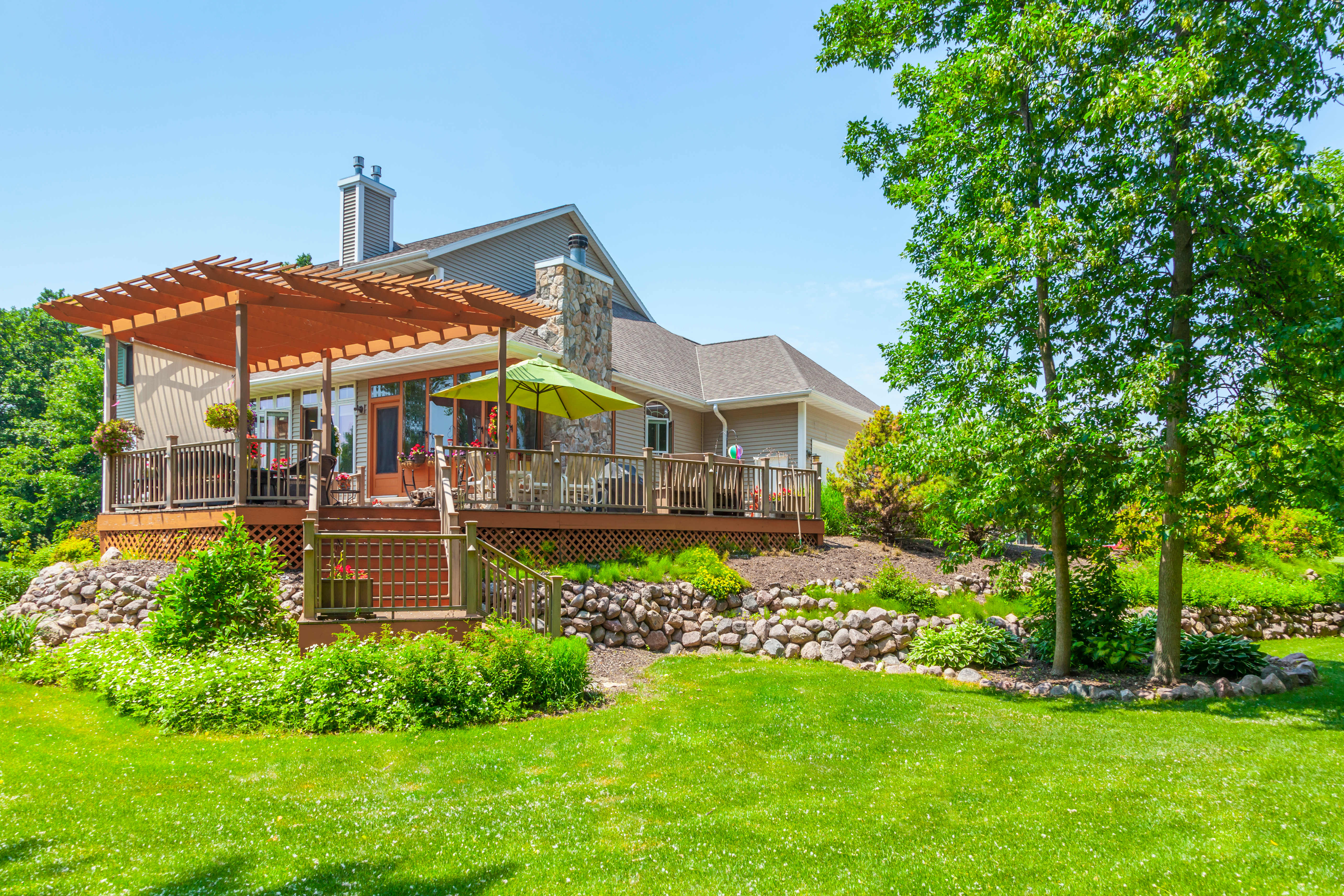 Backyard deck with pergola, outdoor seating, and landscaping surrounded by a lush green lawn.