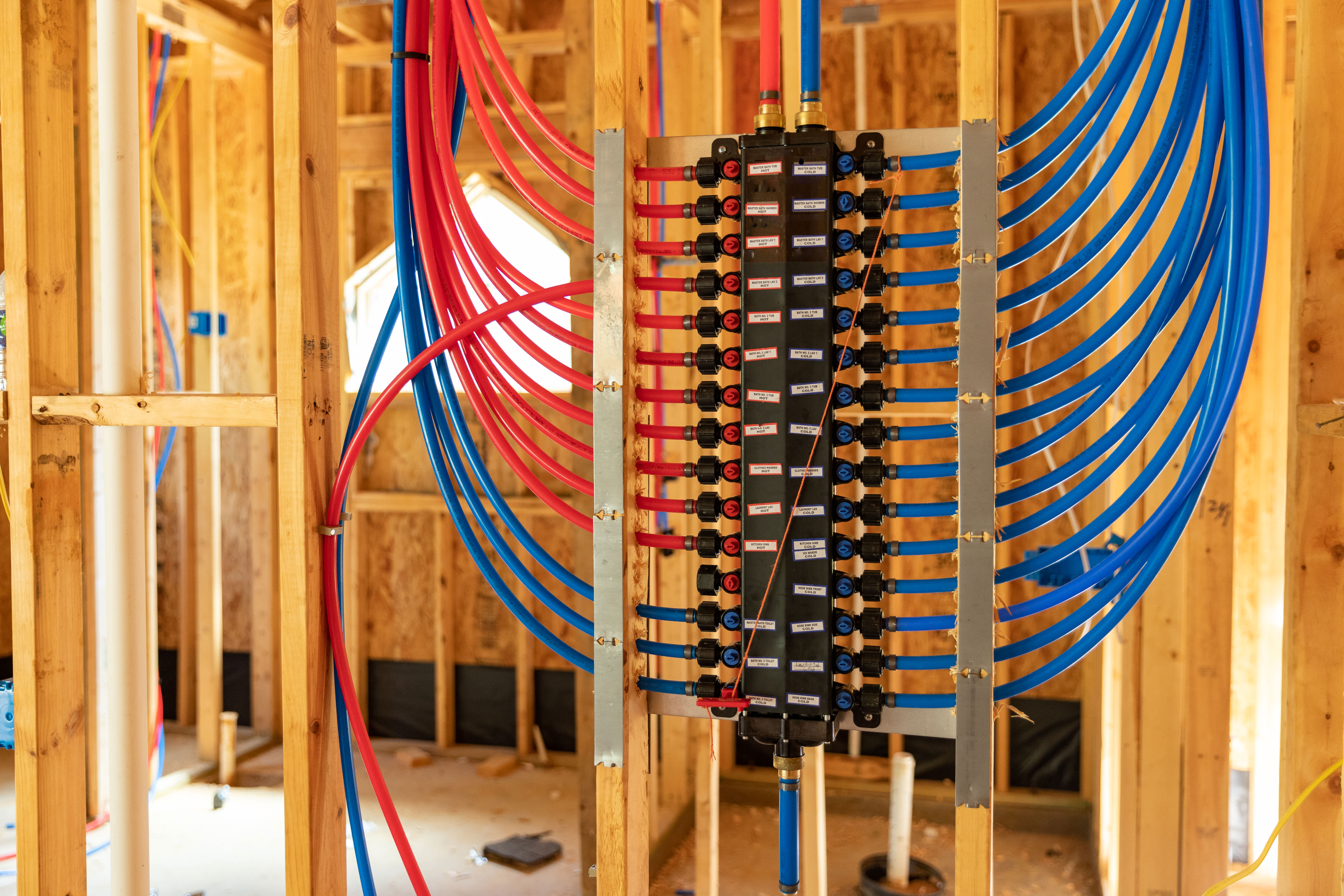 PEX plumbing manifold with red and blue water supply lines installed in a new home under construction.