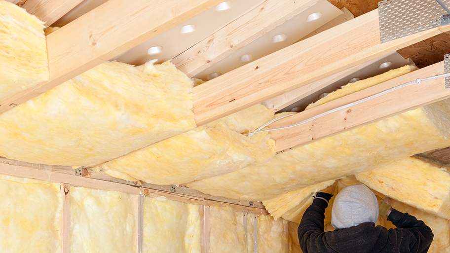 Worker installing fiberglass insulation batts over attic baffles in a house under construction
