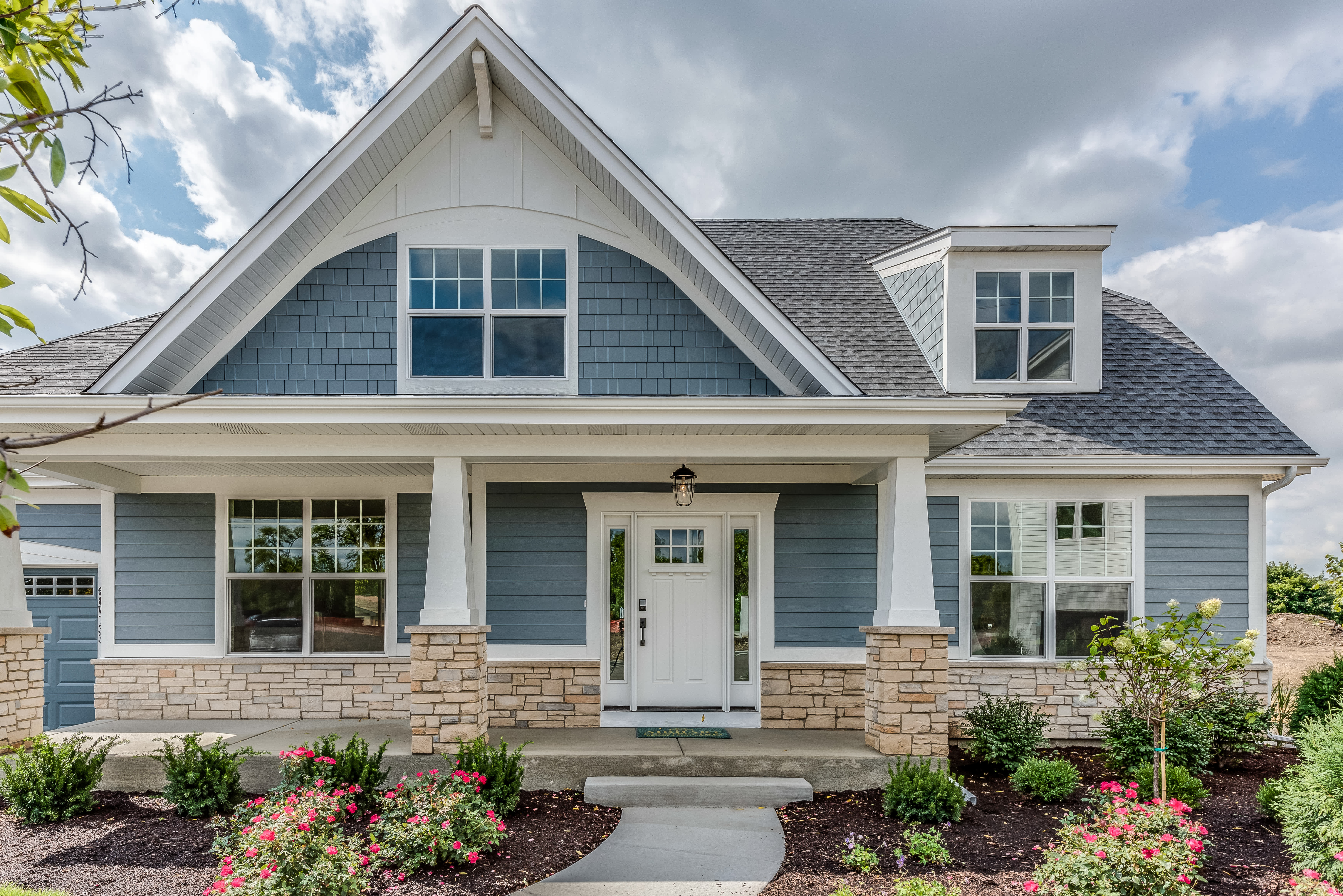 Front view of a modern suburban home with blue siding, stone accents, and a covered porch