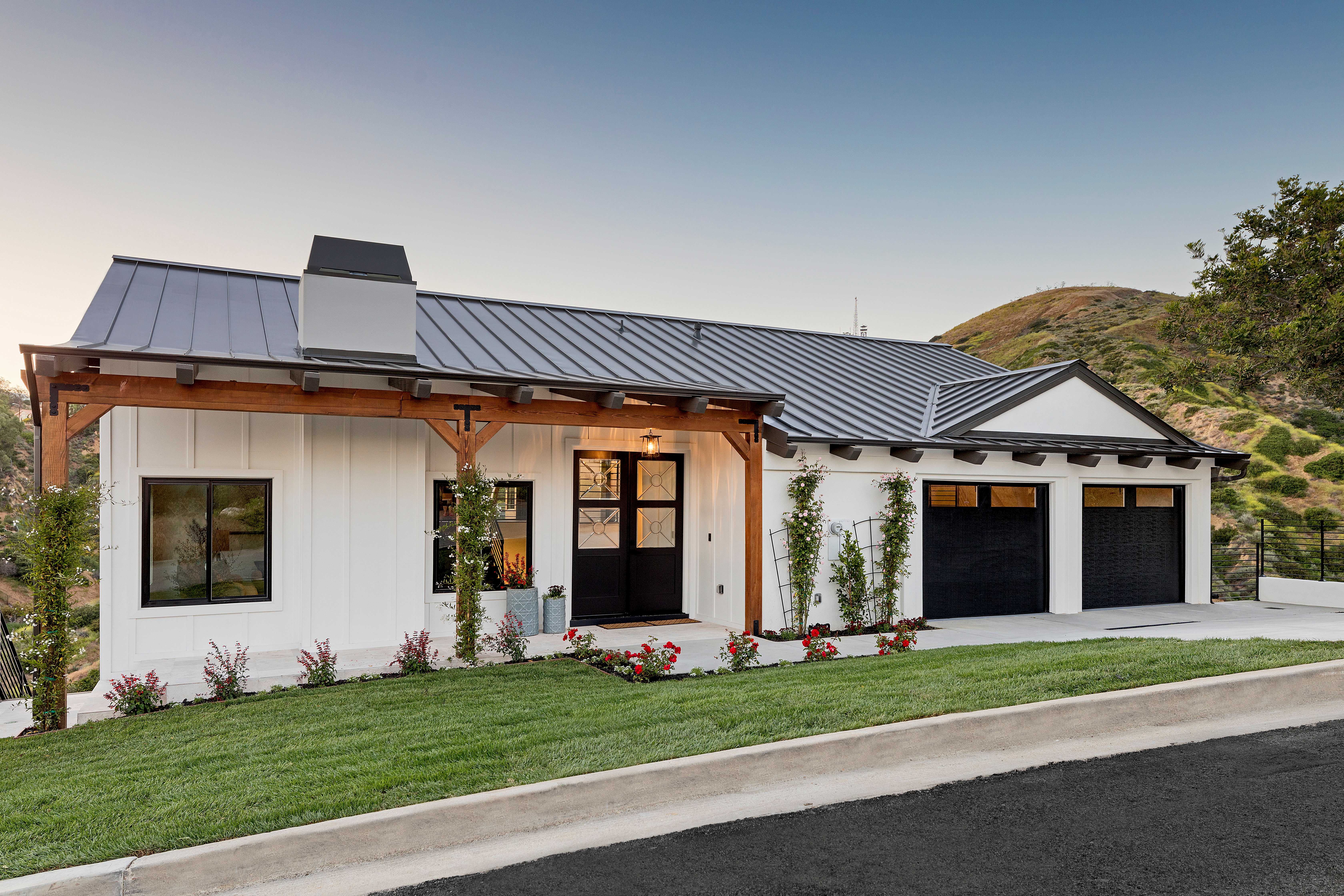 Modern farmhouse with black metal roof, white siding, and a covered entry with wood accents