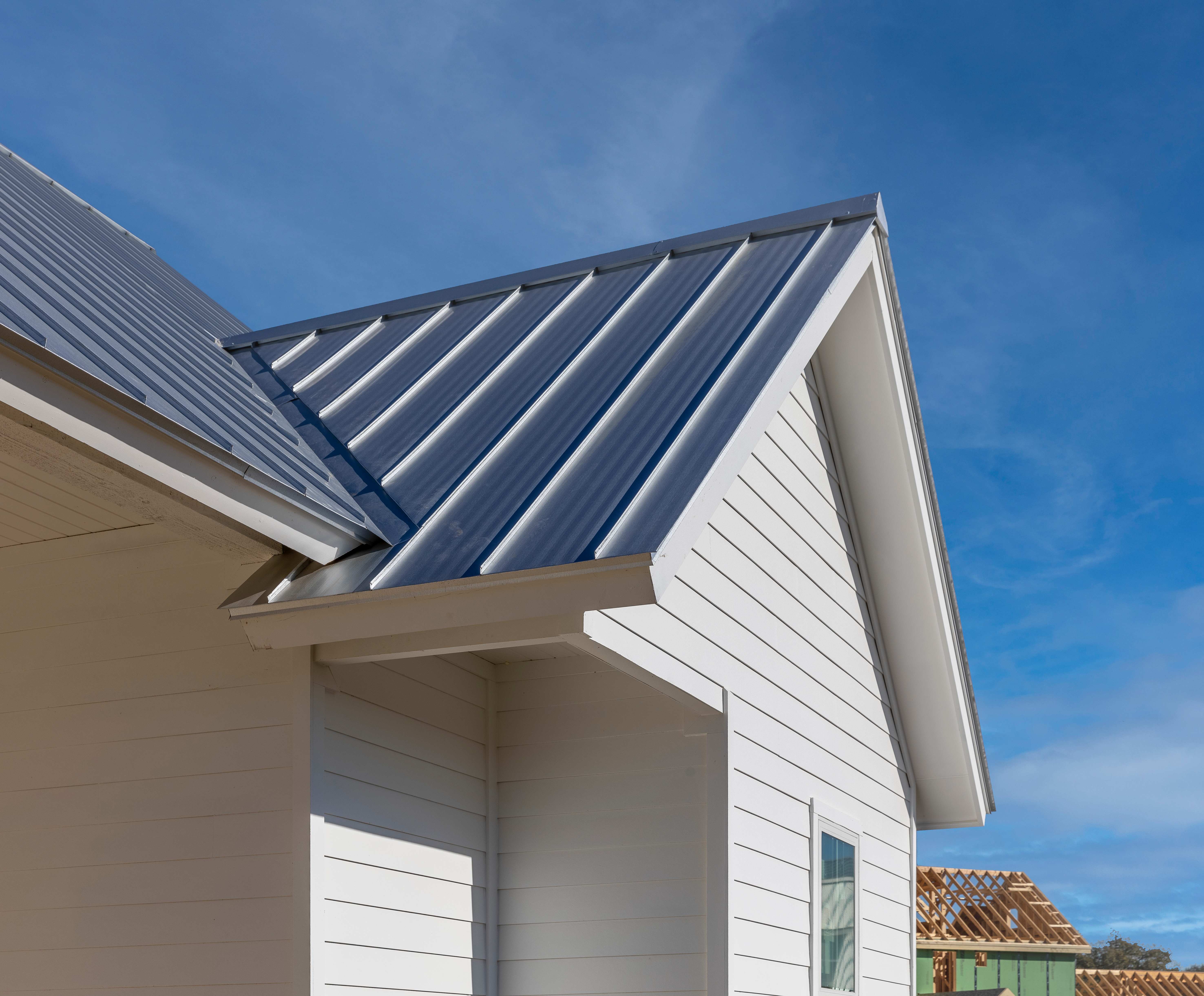 Modern house with a blue standing seam metal roof under a clear sky.
