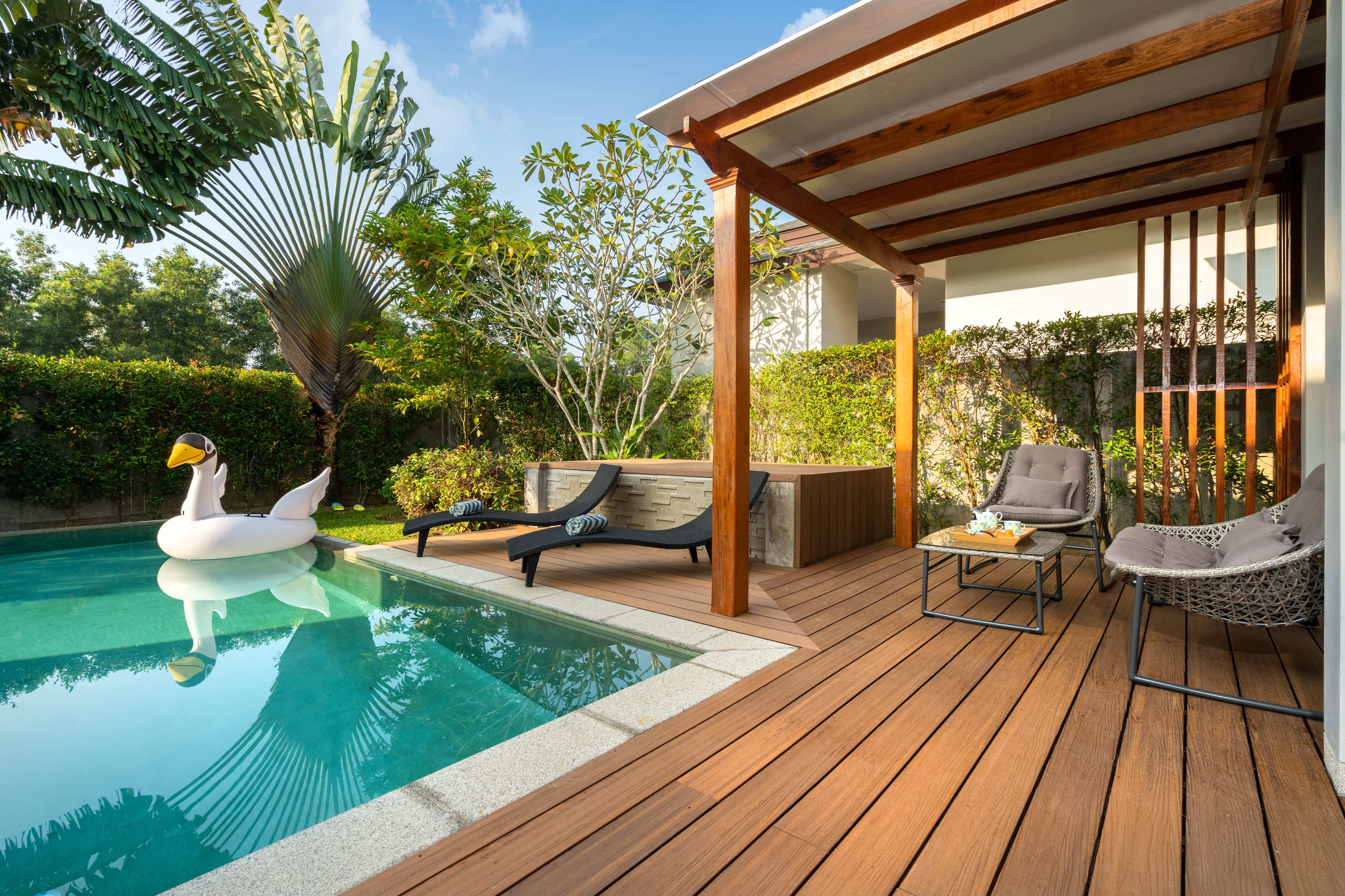 Modern backyard with pool, wood deck, lounge chairs, and covered patio seating