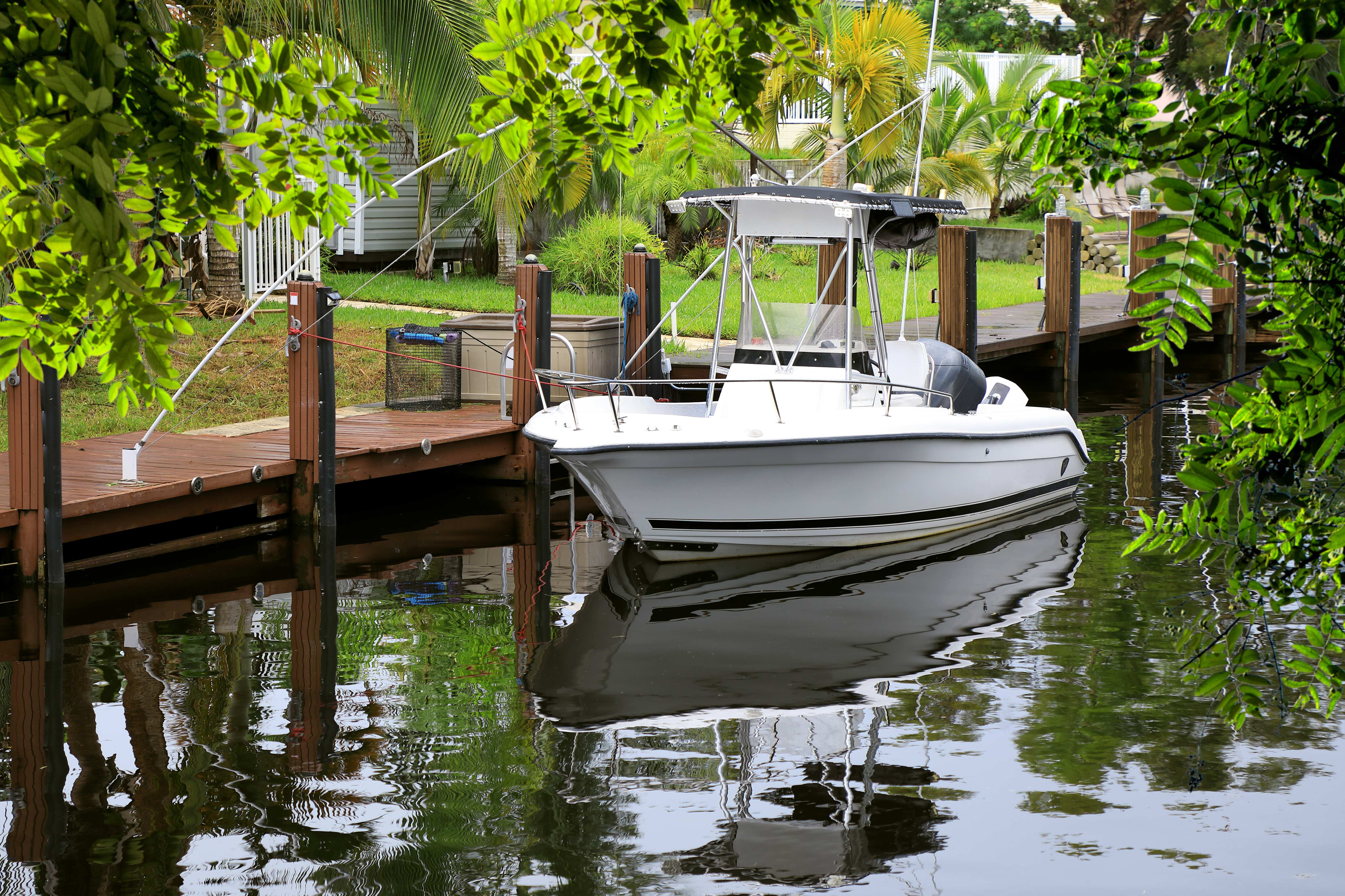 White motorboat docked at a wooden pier surrounded by palm trees and calm water