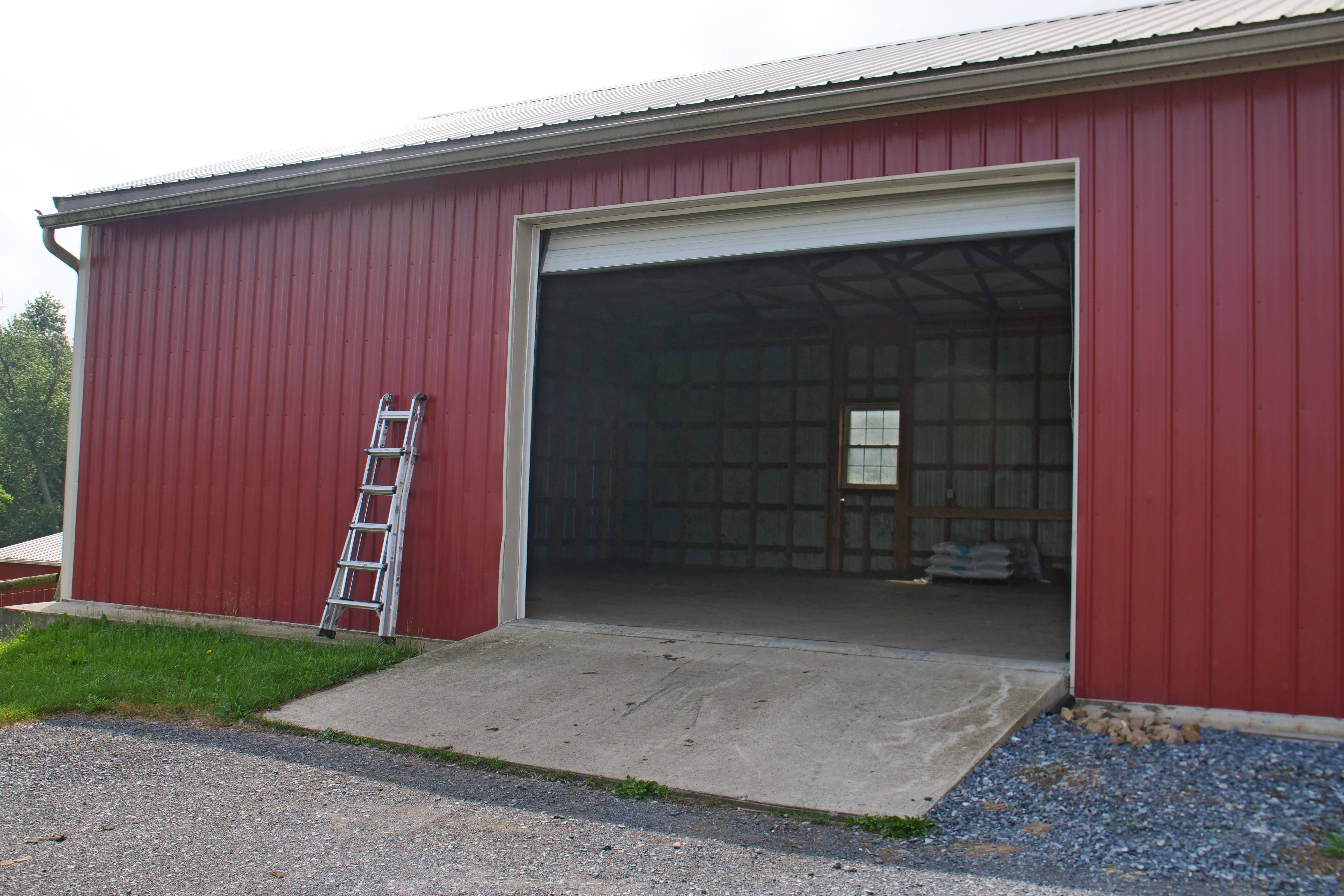 Metal red pole barn with a white roof and open garage door