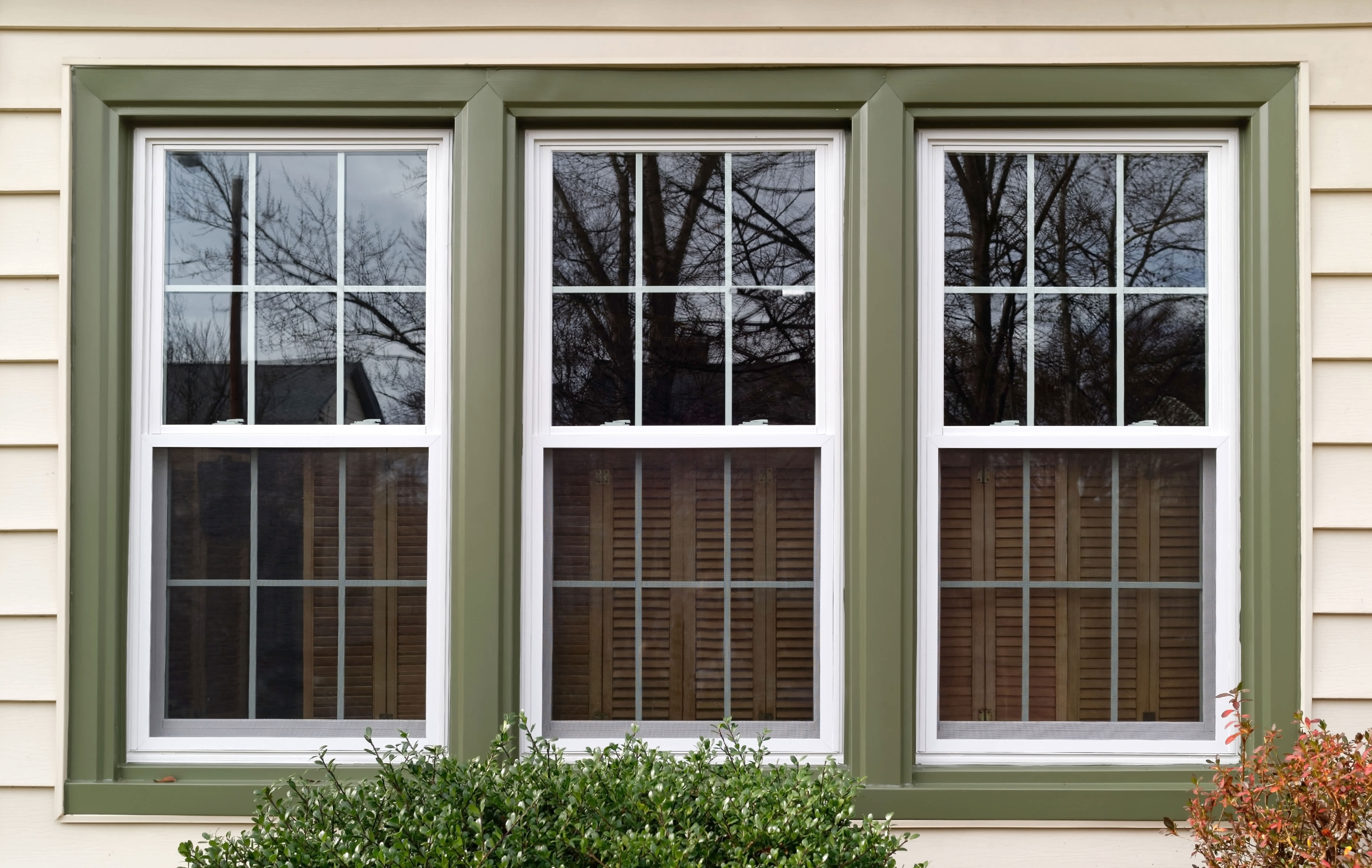 Three double-hung windows with green trim on a beige house exterior.