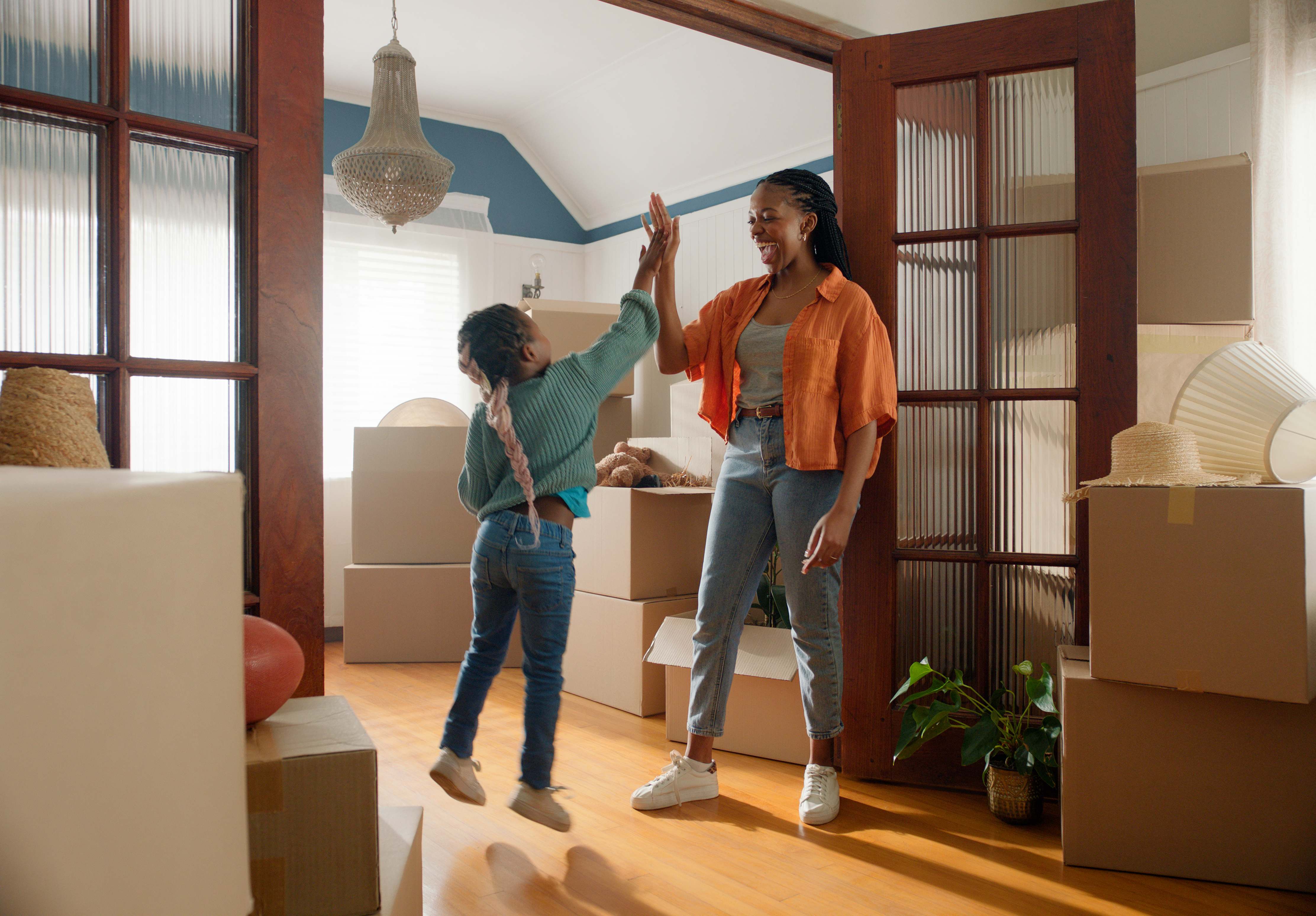 Mother and daughter celebrating with a high five while unpacking boxes in their new home