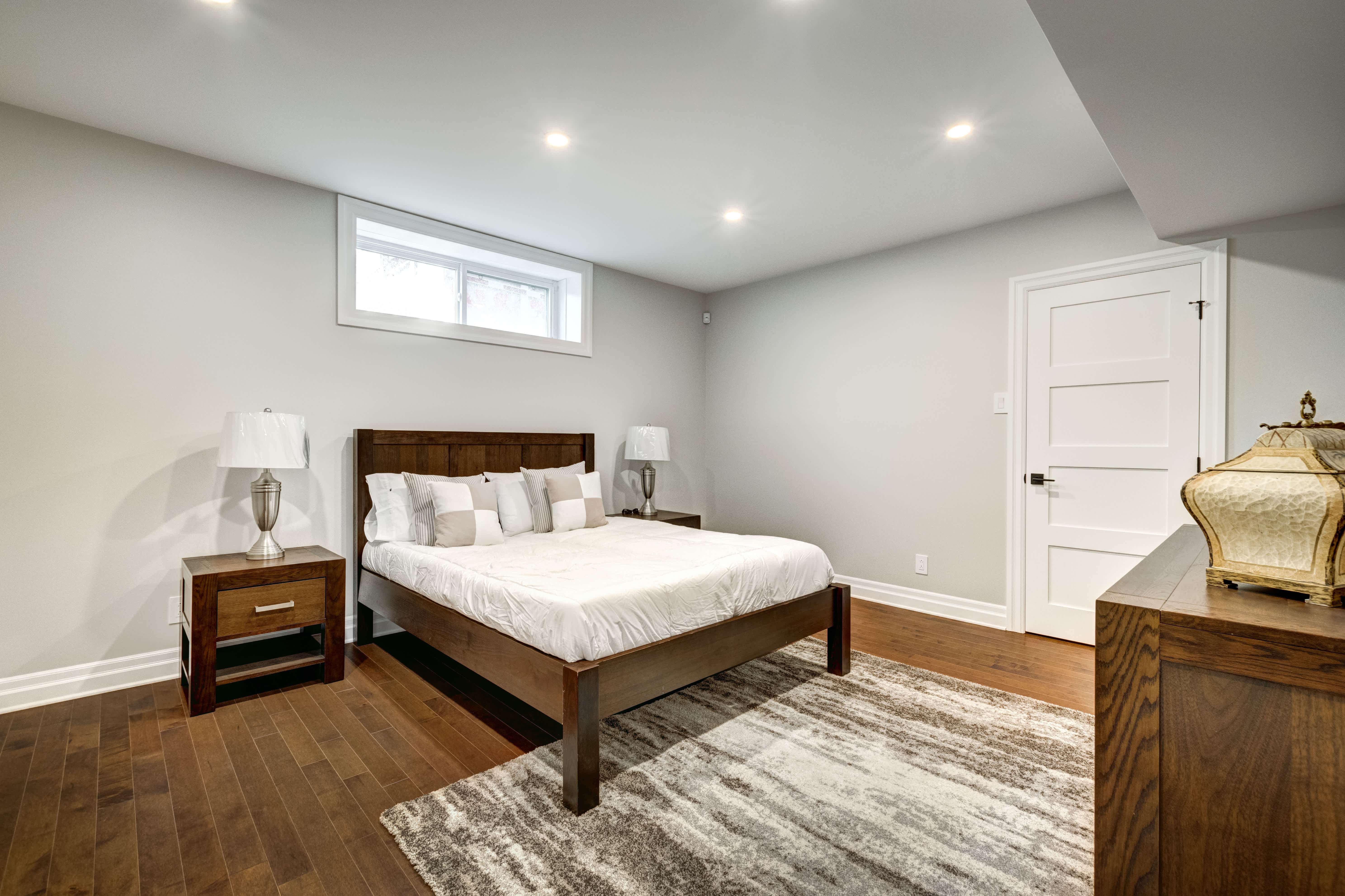 Bedroom in basement with wooden bed frame and rug on hardwood floors