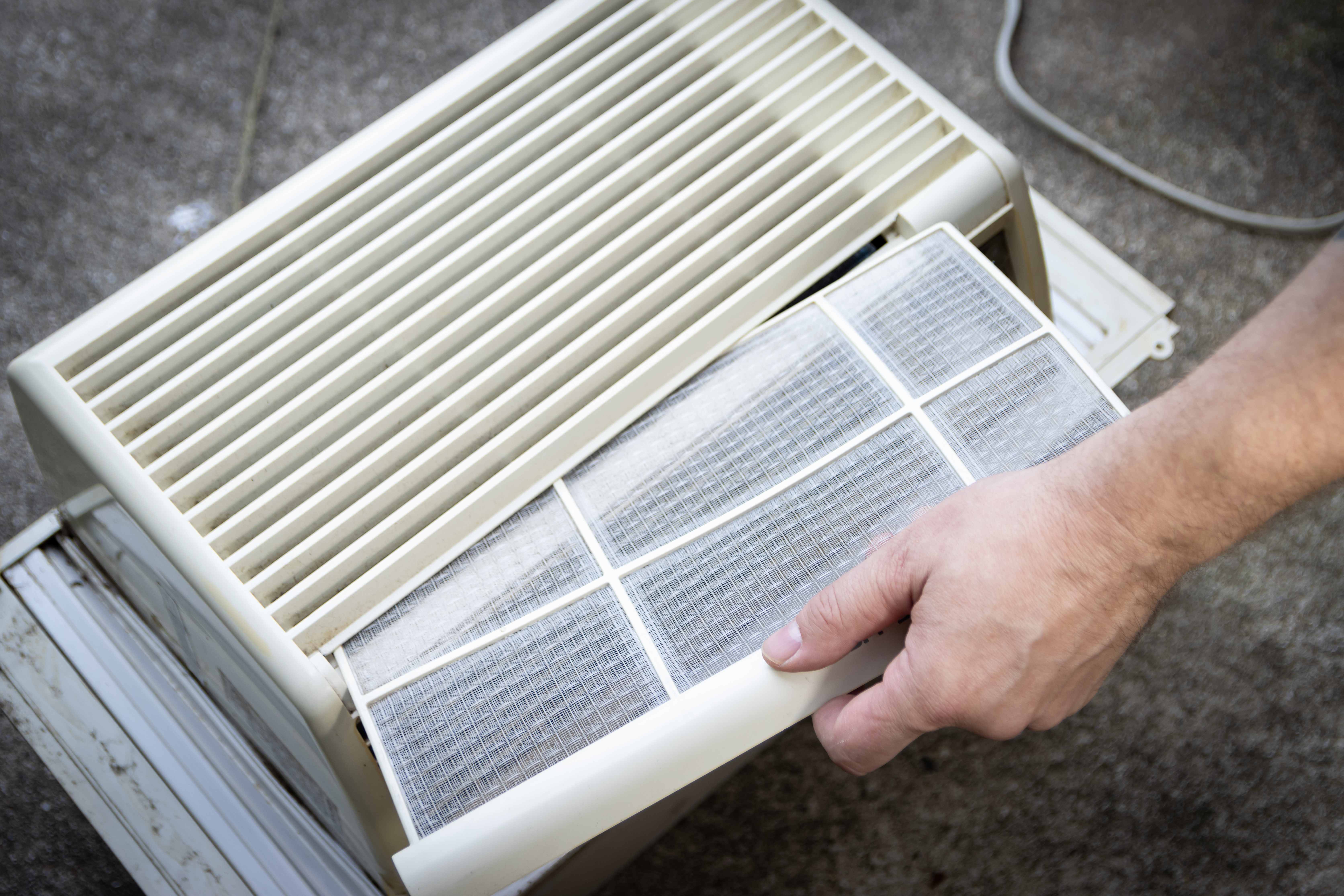 Person replaces an air filter from a window air conditioning unit