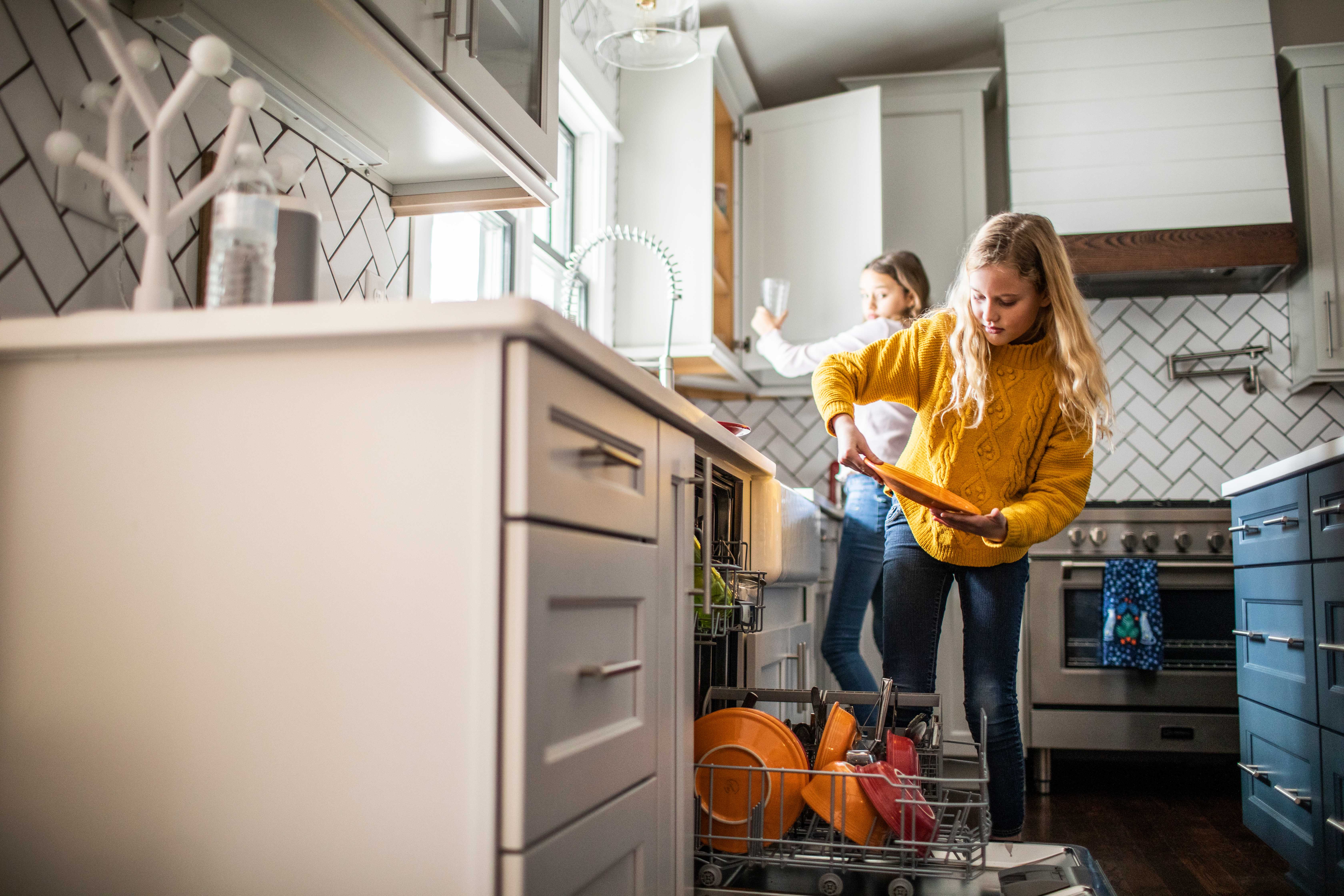 Two young girls putting away dishes from dishwasher in modern kitchen