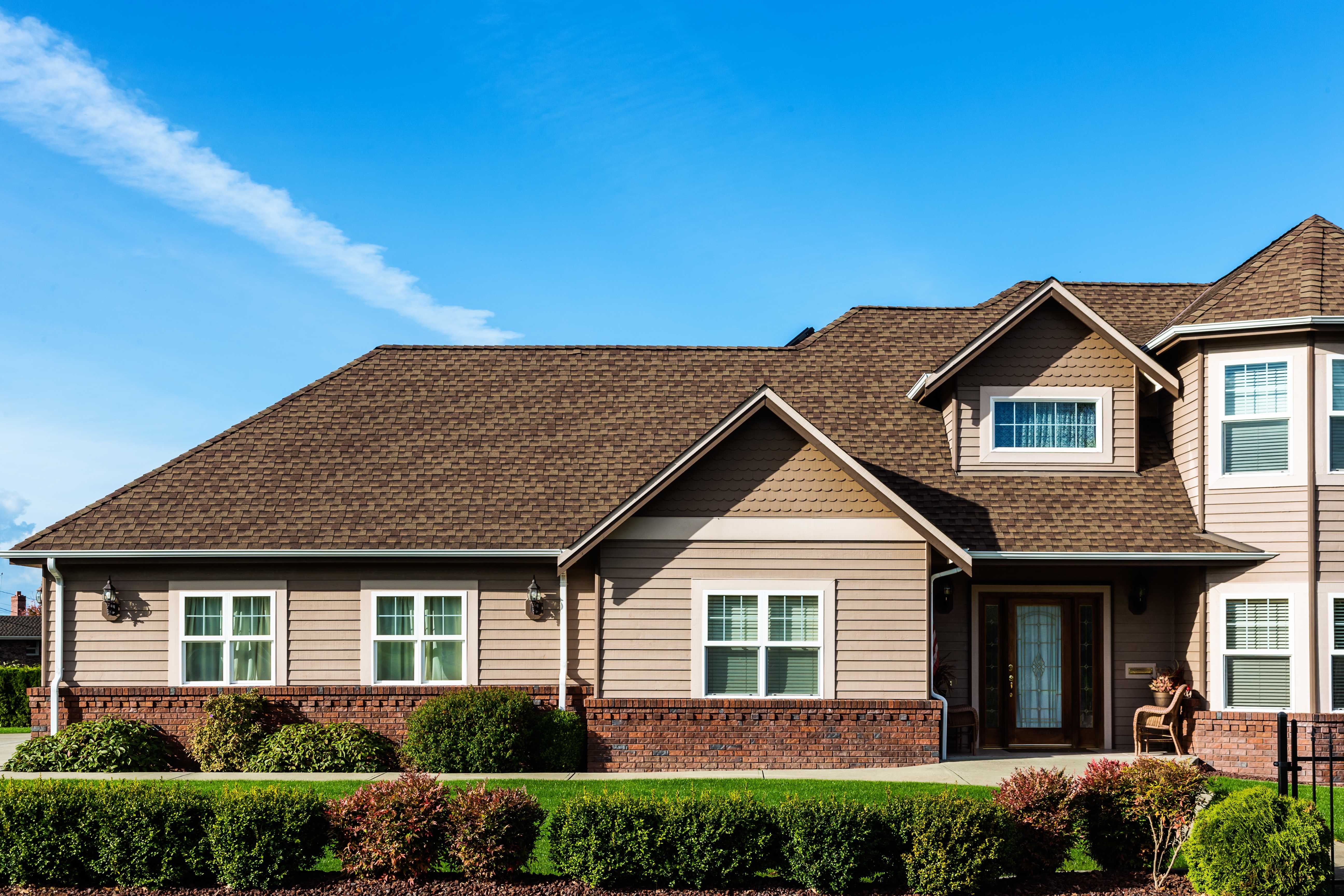 Modern American home exterior with large windows, stone accents, manicured lawn, and bright evening lighting