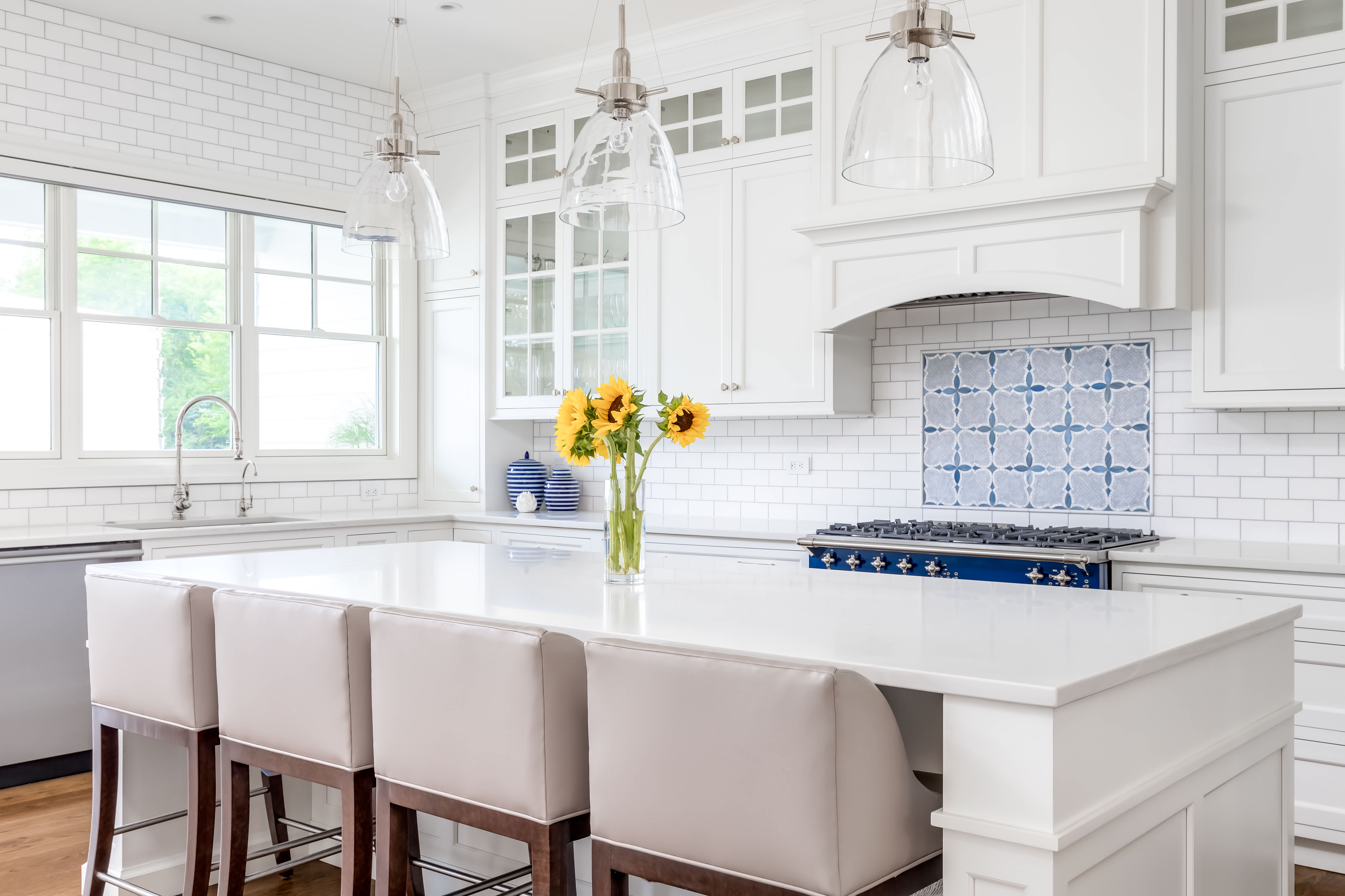 Bright white kitchen with large island, bar stools, pendant lights, and tiled backsplash creating a modern clean look