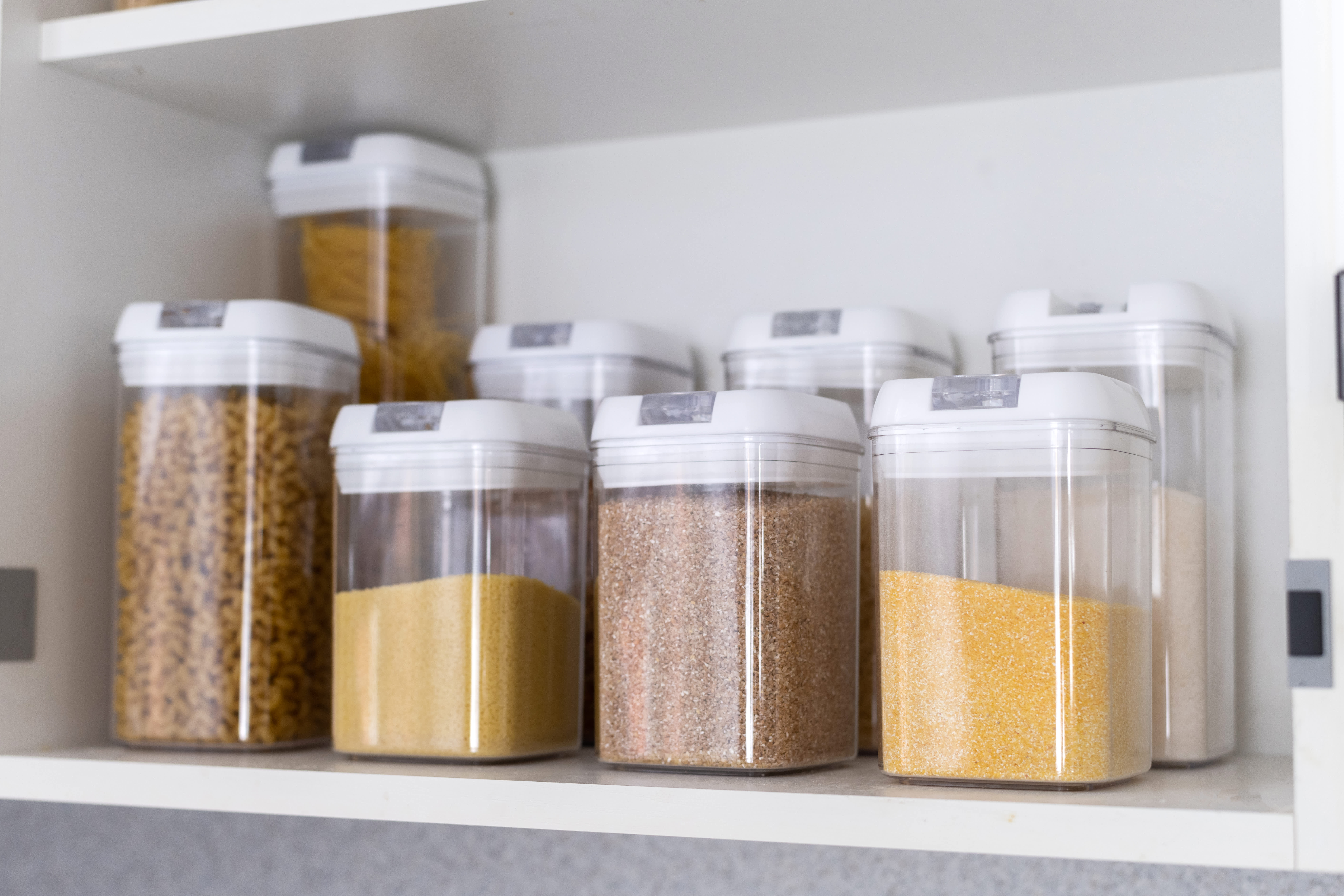 Neatly organized food storage containers on white kitchen shelves, showcasing clean, modern, and efficient organization
