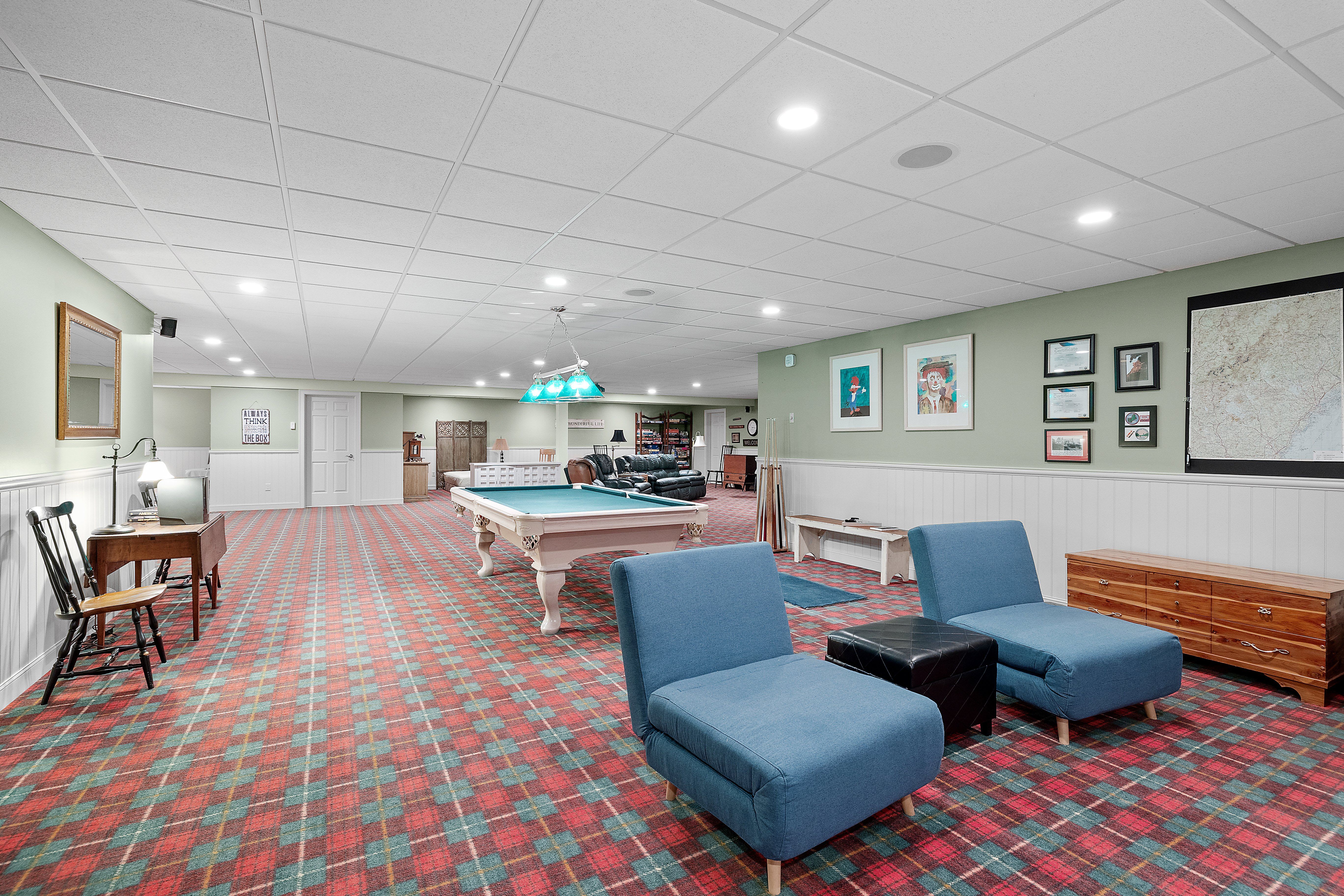 Spacious basement with red and green plaid carpet, pool table, lounge chairs, and framed artwork on the walls