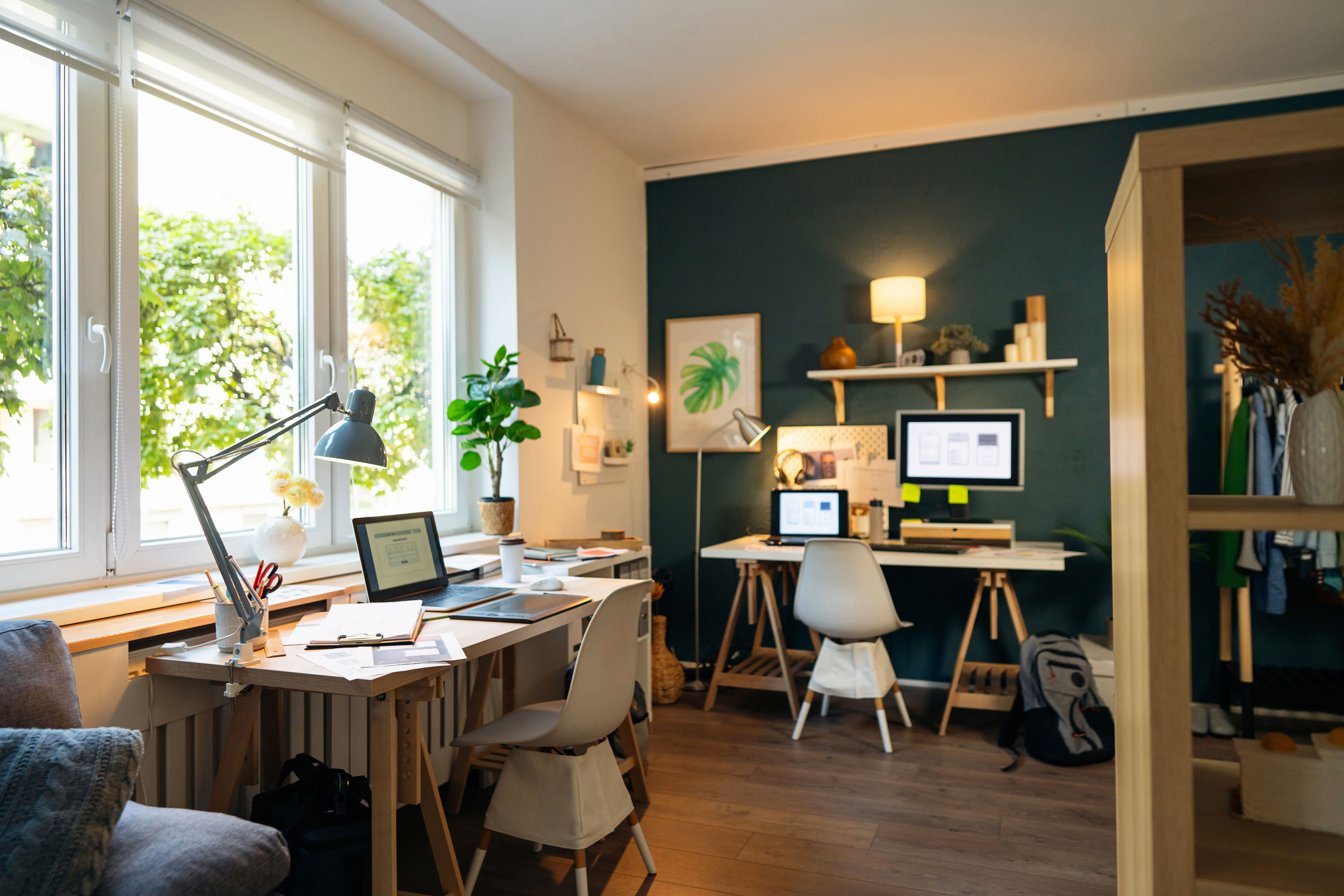 Cozy home office with two desks, laptops, lamps, plants, and shelves against a dark accent wall