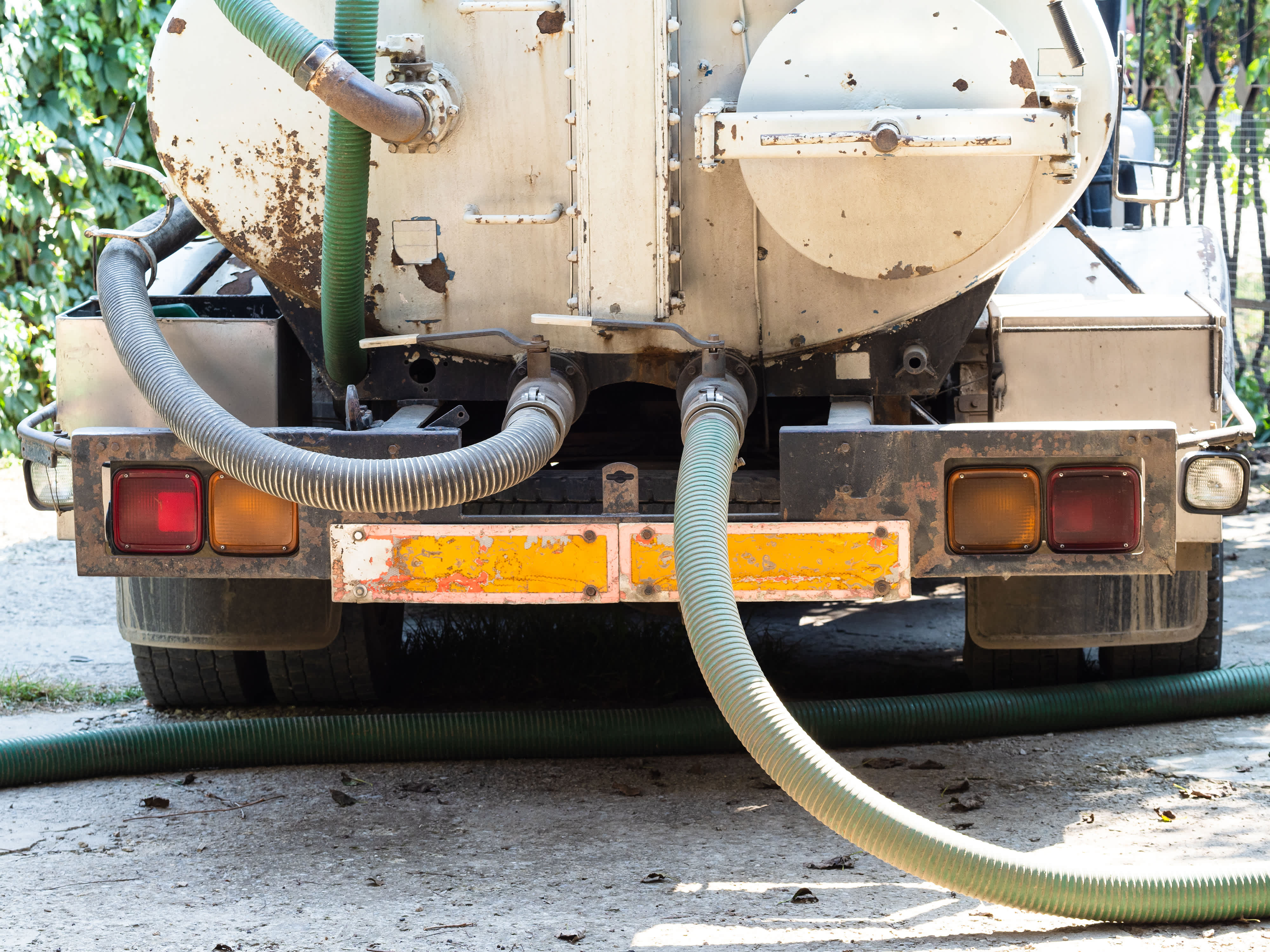 Rear view of a septic tank truck with large suction hoses attached for pumping waste.